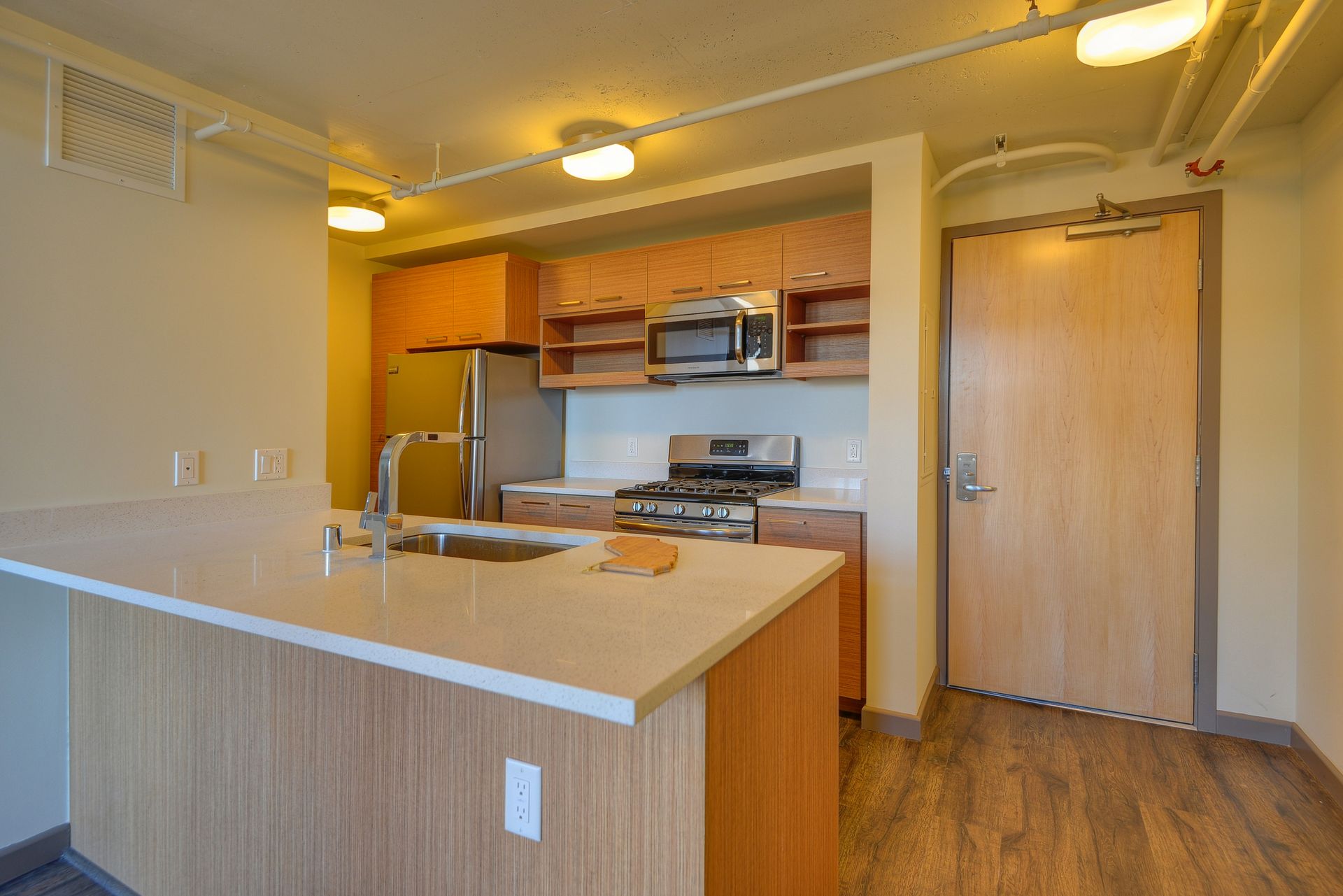 Empty apartment kitchen with wood cabinets, white countertops, and stainless steel appliances