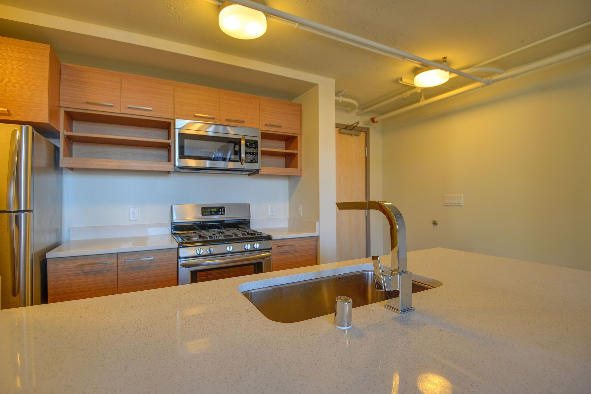 Empty modern kitchen with wood cabinets, stainless appliances, and a large island sink