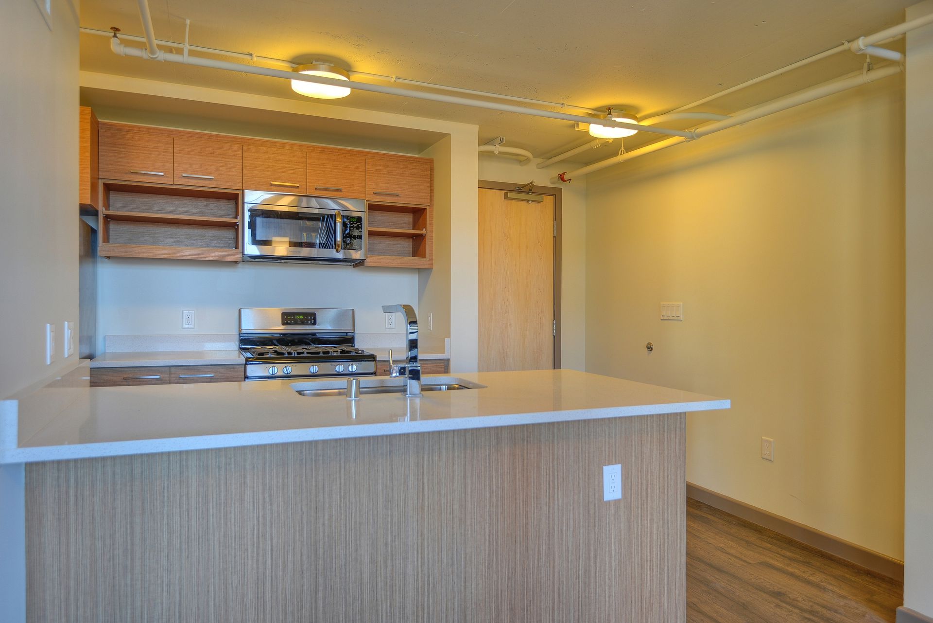 Empty modern kitchen with light wood cabinets, white island countertop, and hardwood floors