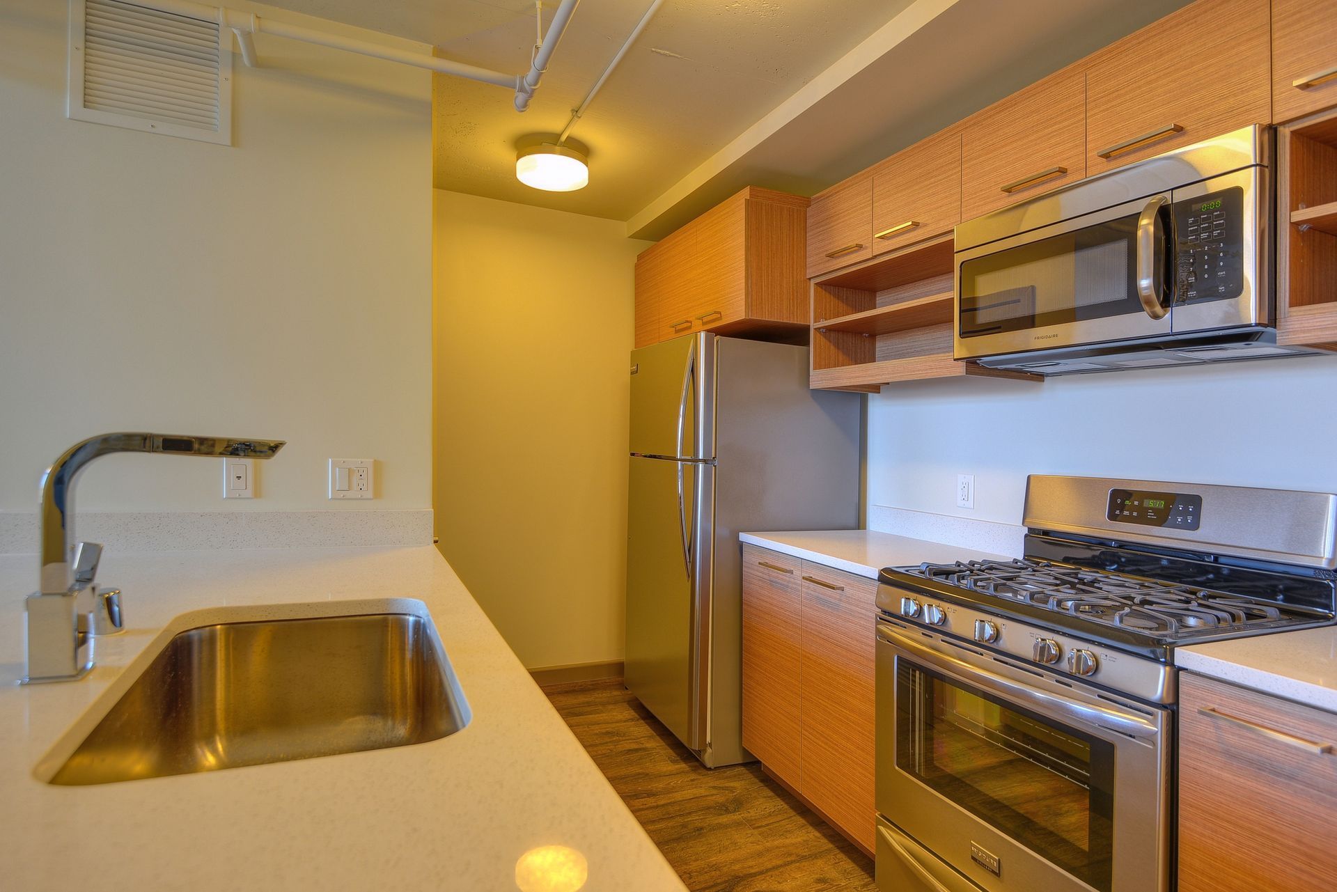 Compact modern kitchen with stainless steel appliances, wood cabinets, and white countertop with sink