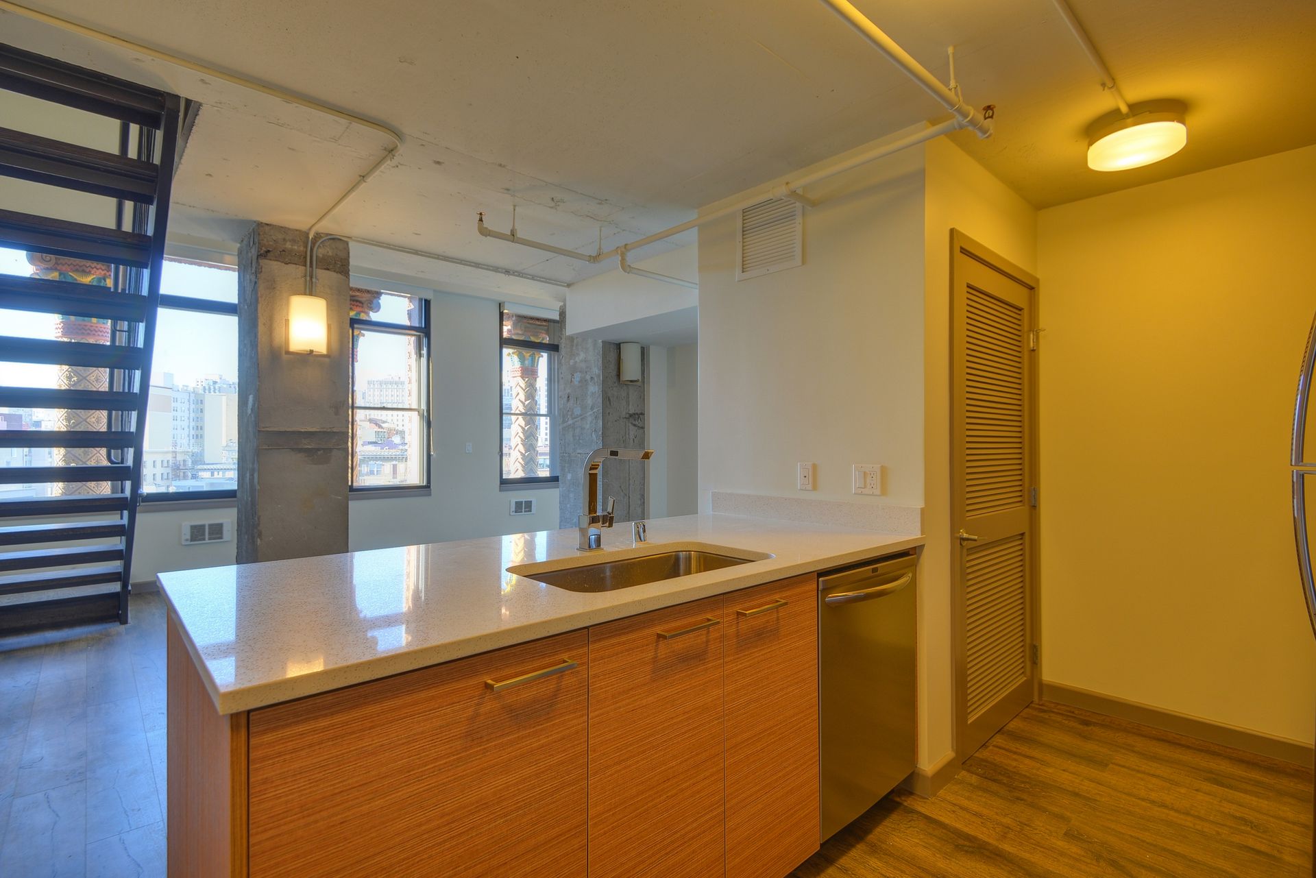 Modern apartment kitchen with island, white countertops, wooden cabinets, and large windows.