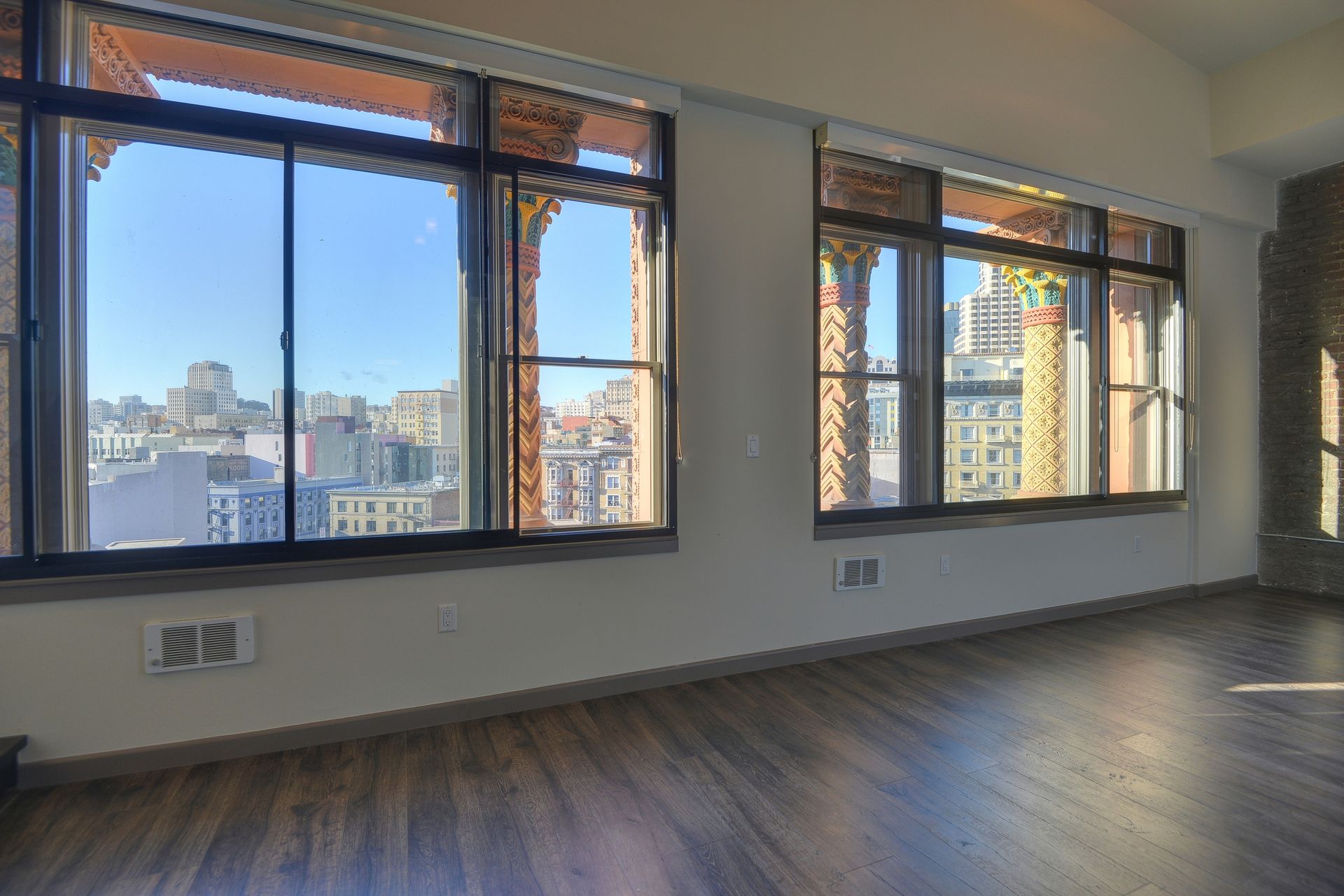 Empty modern apartment room with large windows, city view, and wood floors