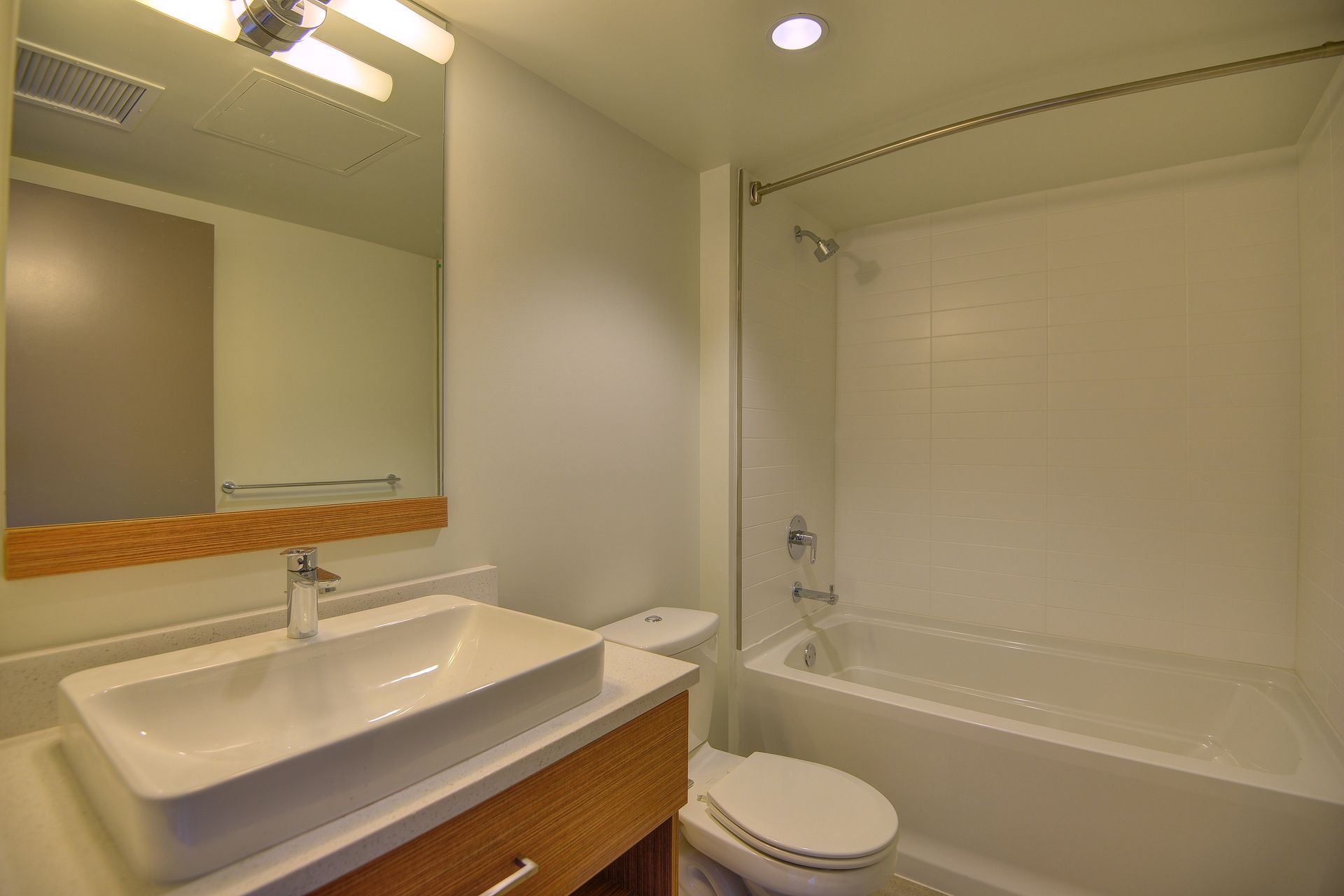 Bathroom with a sink, mirror, toilet, and bathtub with white tile surround.