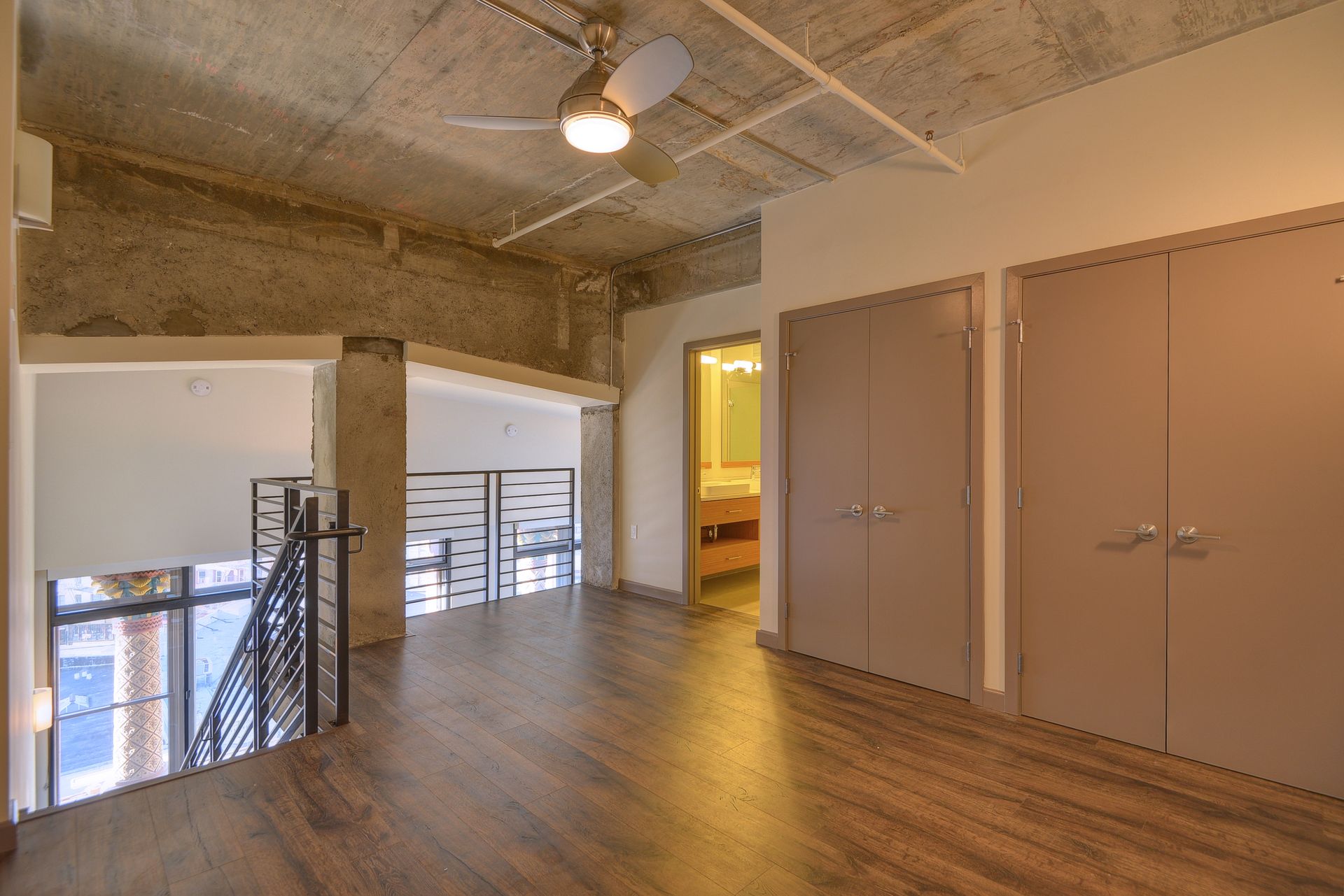 Modern loft interior with wood floor, exposed concrete ceiling, and double doors beside a stair railing