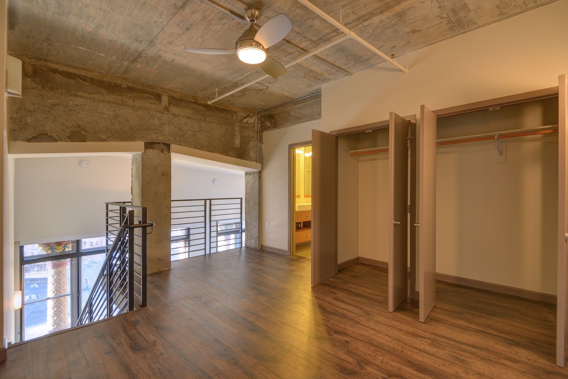 Modern loft interior with wood floors, exposed ceiling, balcony railing, and open closet area