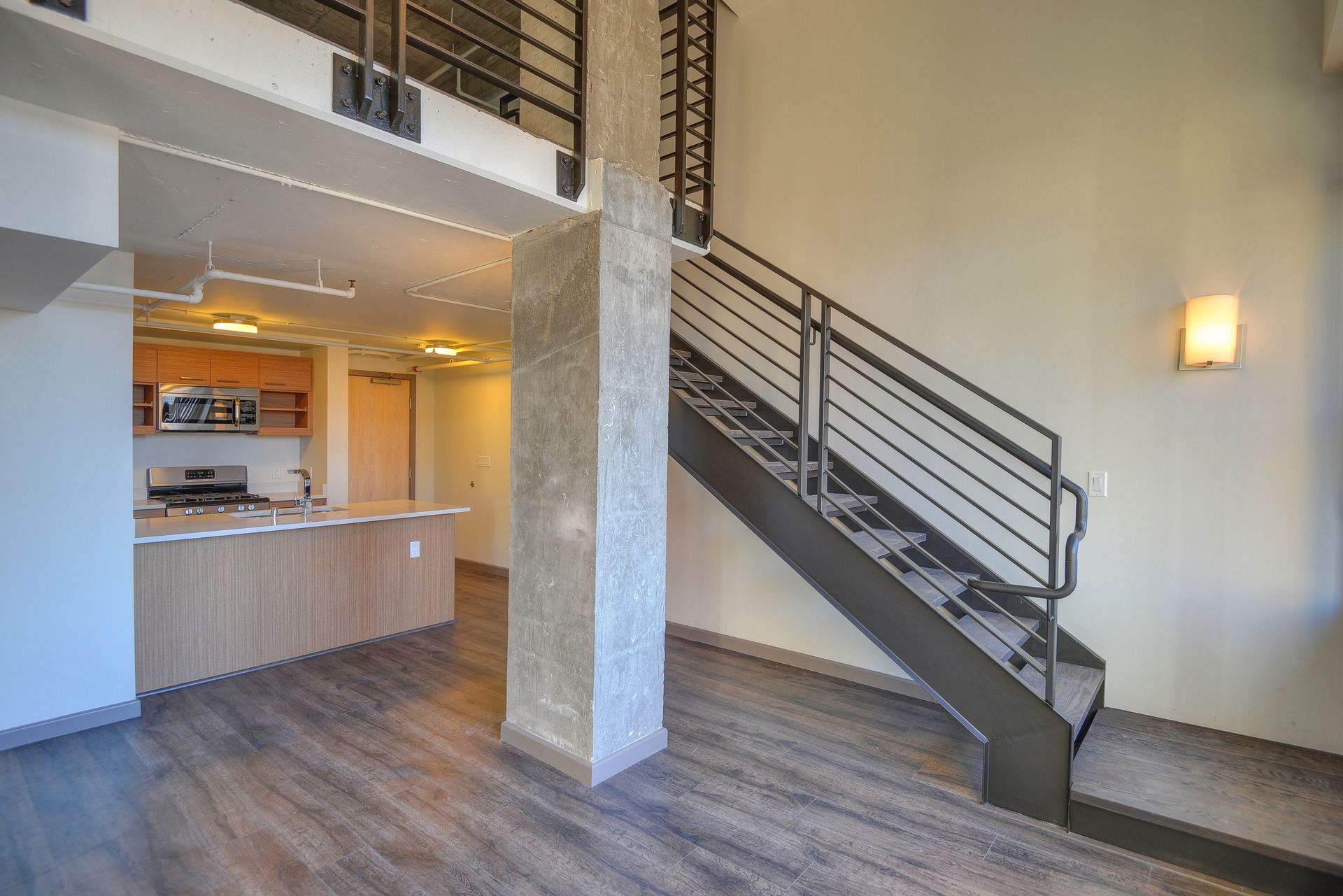 Modern apartment interior with wood floors, staircase, kitchen, and high ceiling