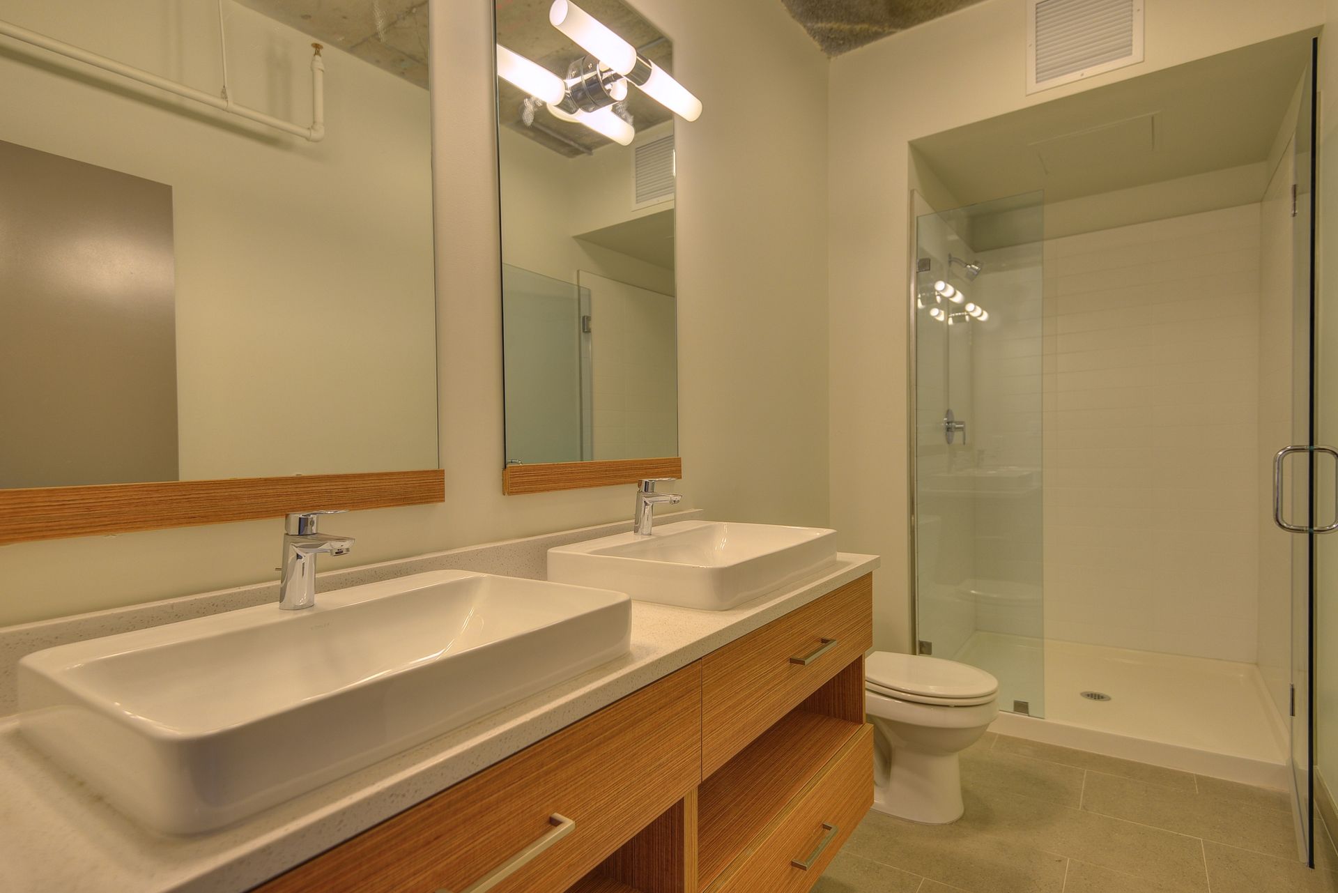 Modern bathroom with double sinks, large mirrors, and a glass-enclosed shower