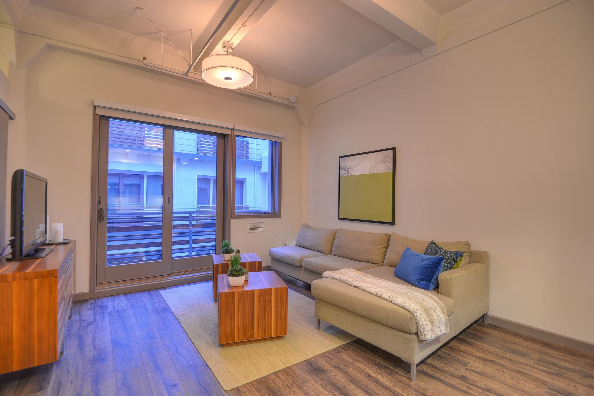 Modern living room with a beige sofa, coffee table, wall art, and large window overlooking a balcony.
