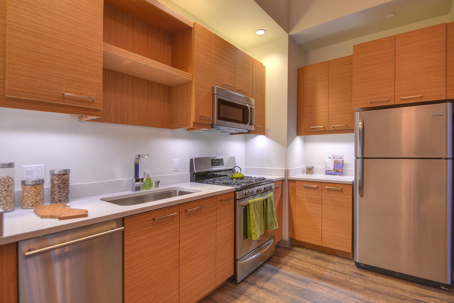 Compact modern kitchen with wooden cabinets, stainless steel appliances, and light countertops