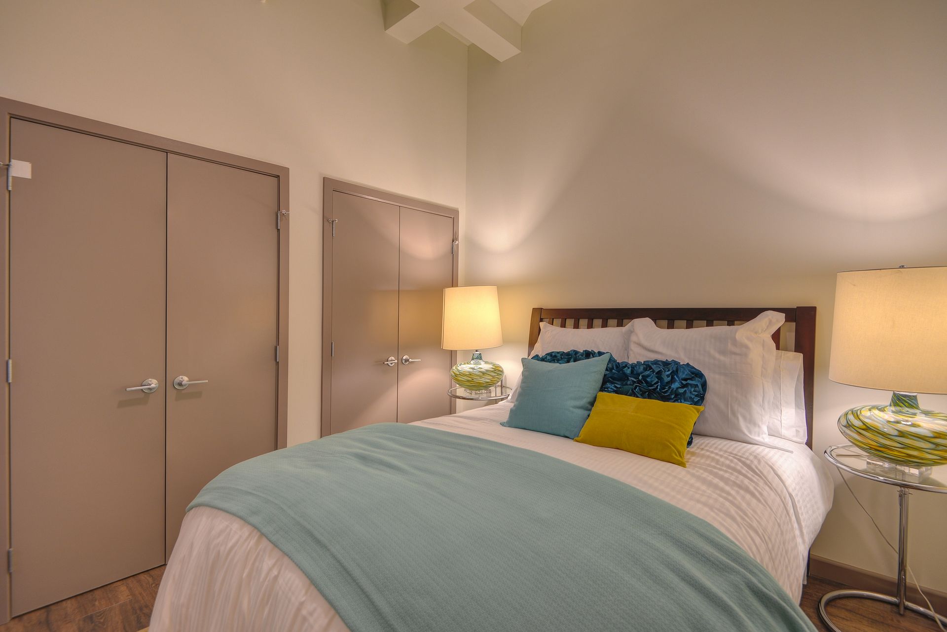 Cozy bedroom with a bed, teal throw, yellow pillow, lamp, and mirrored side table