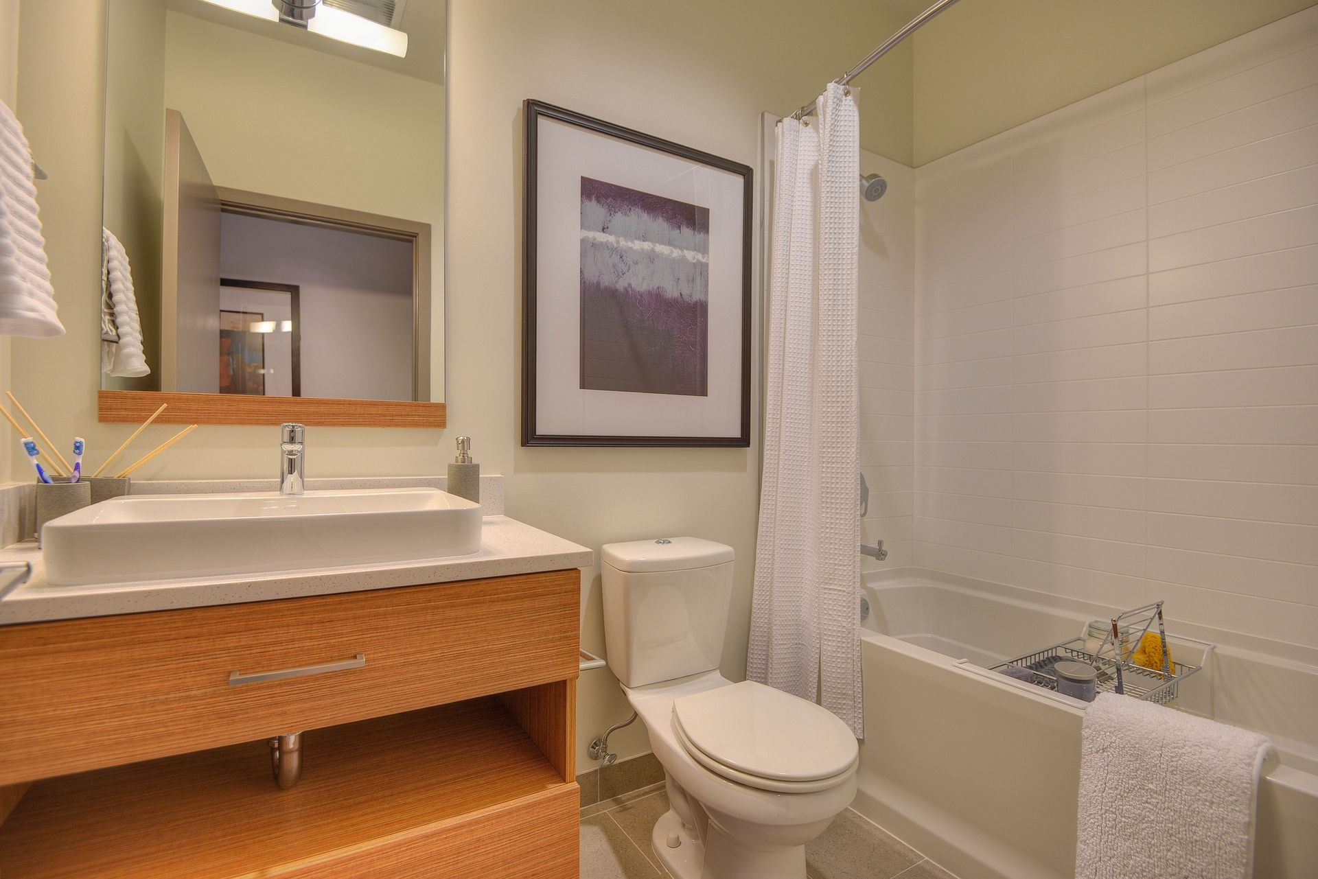 Small beige bathroom with sink, toilet, bathtub, mirror, and shower curtain.
