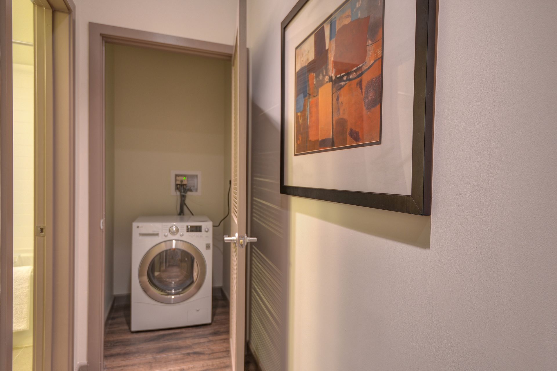 Hallway view of a laundry nook with a front-load washer and framed wall art.
