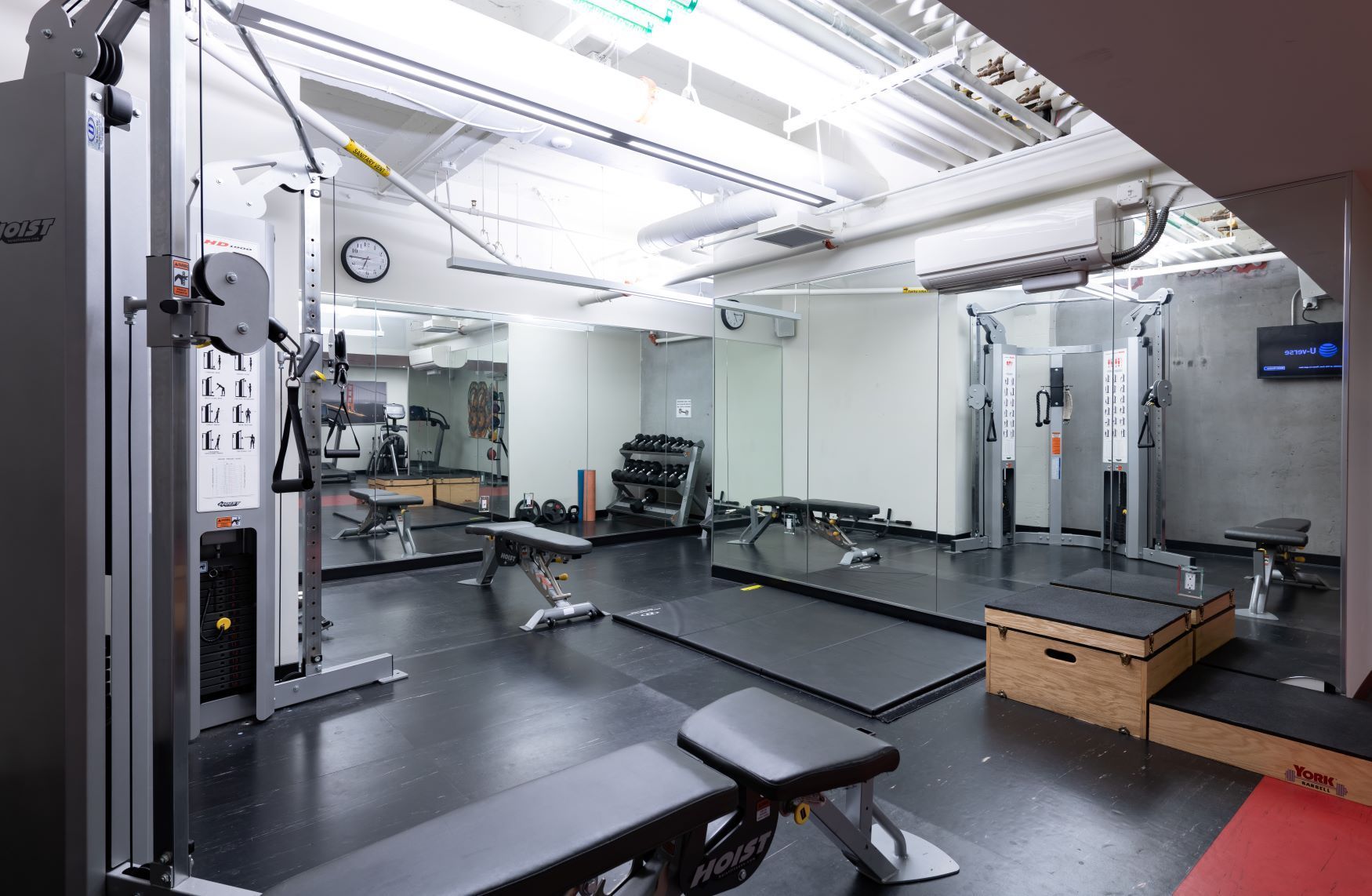 Modern gym with cable machines, benches, mirrors, and bright overhead lighting.