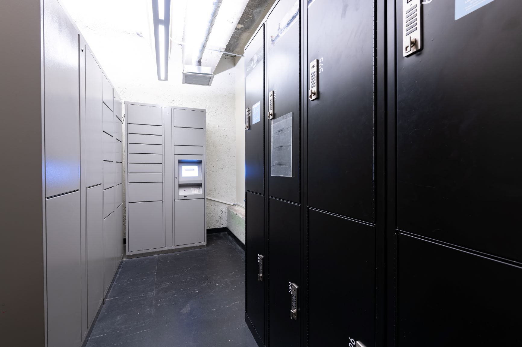 Narrow server room aisle with black equipment racks, gray cabinets, and bright overhead lights