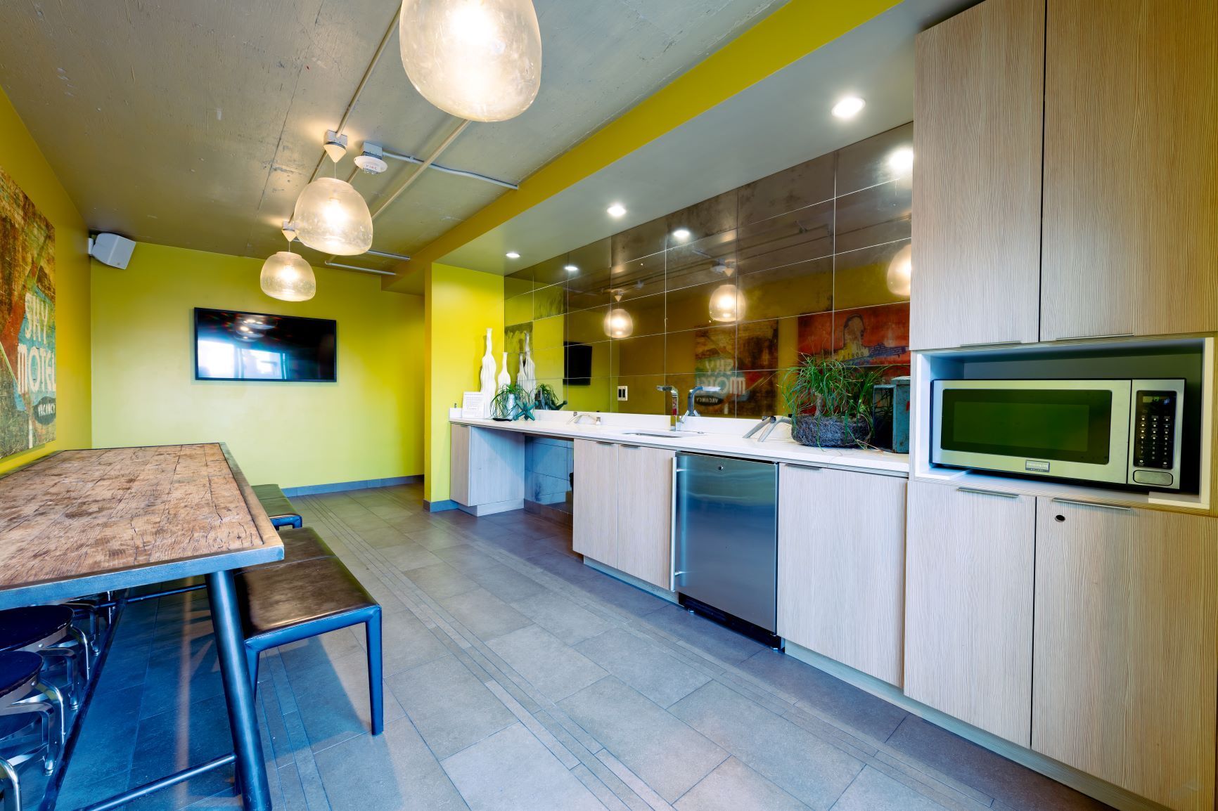 Modern kitchen with yellow walls, wood cabinets, stainless appliances, and a dining table by hanging lights