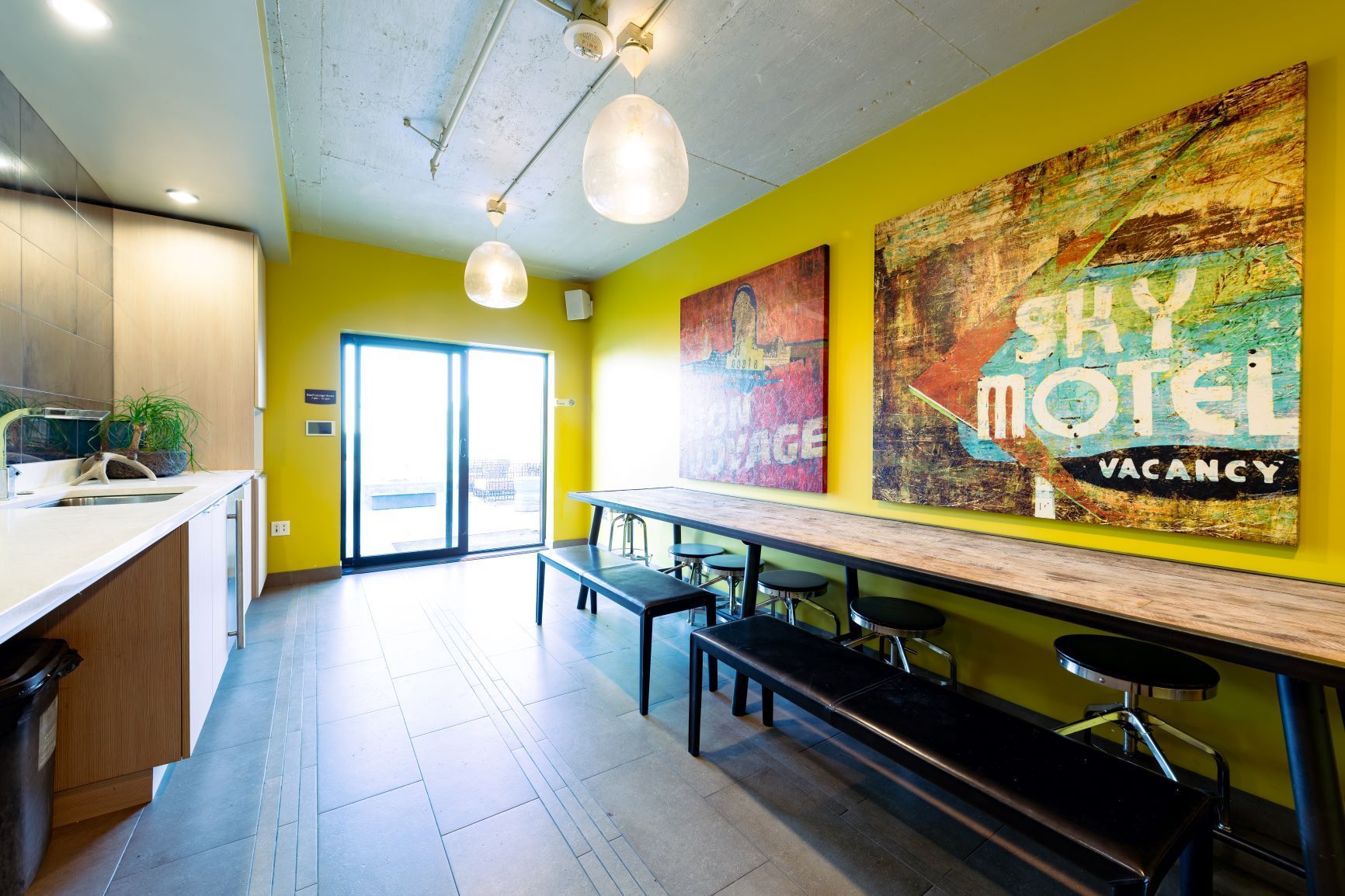 Bright motel lobby with lime-green walls, pendant lights, benches, and “SLEEP MOTEL VACANCY” wall art