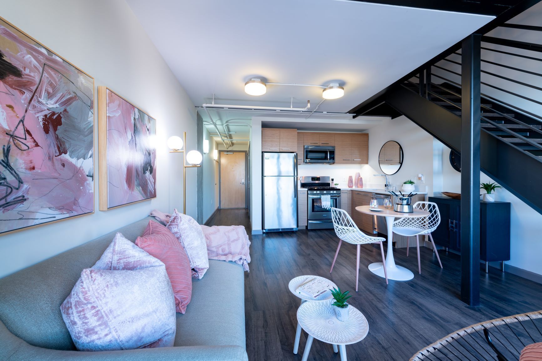 Modern living room with gray sofa, pink pillows, staircase, and dining area in an open loft