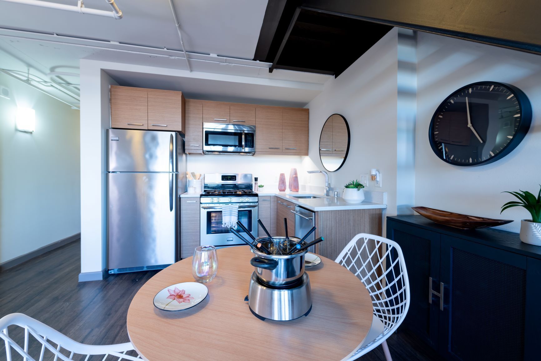 Modern kitchen and dining nook with stainless appliances, round table, and black wall clock