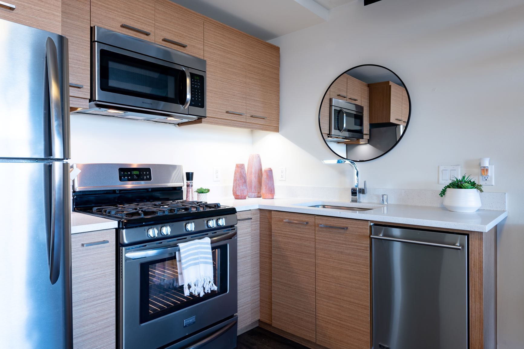 Modern kitchen with stainless steel appliances, wood cabinets, and round mirror above the sink.