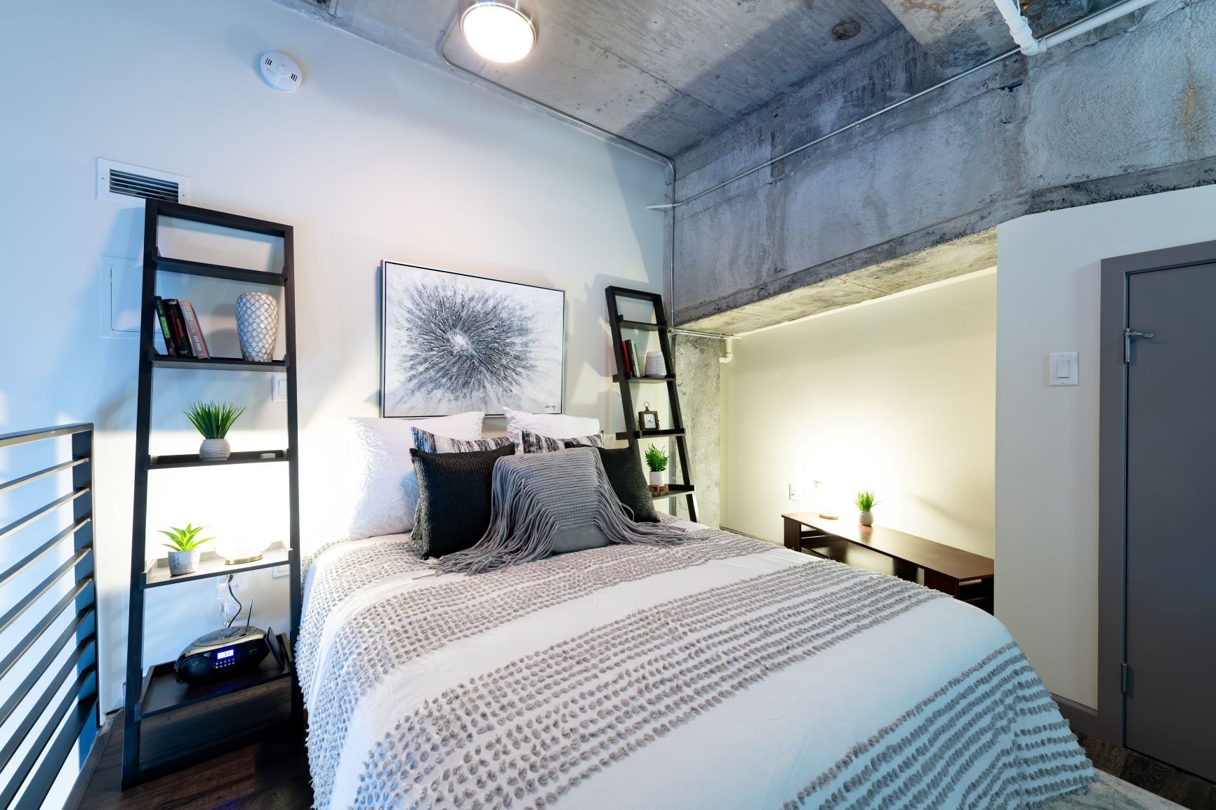 Modern bedroom with bed, ladder shelves, and industrial concrete ceiling