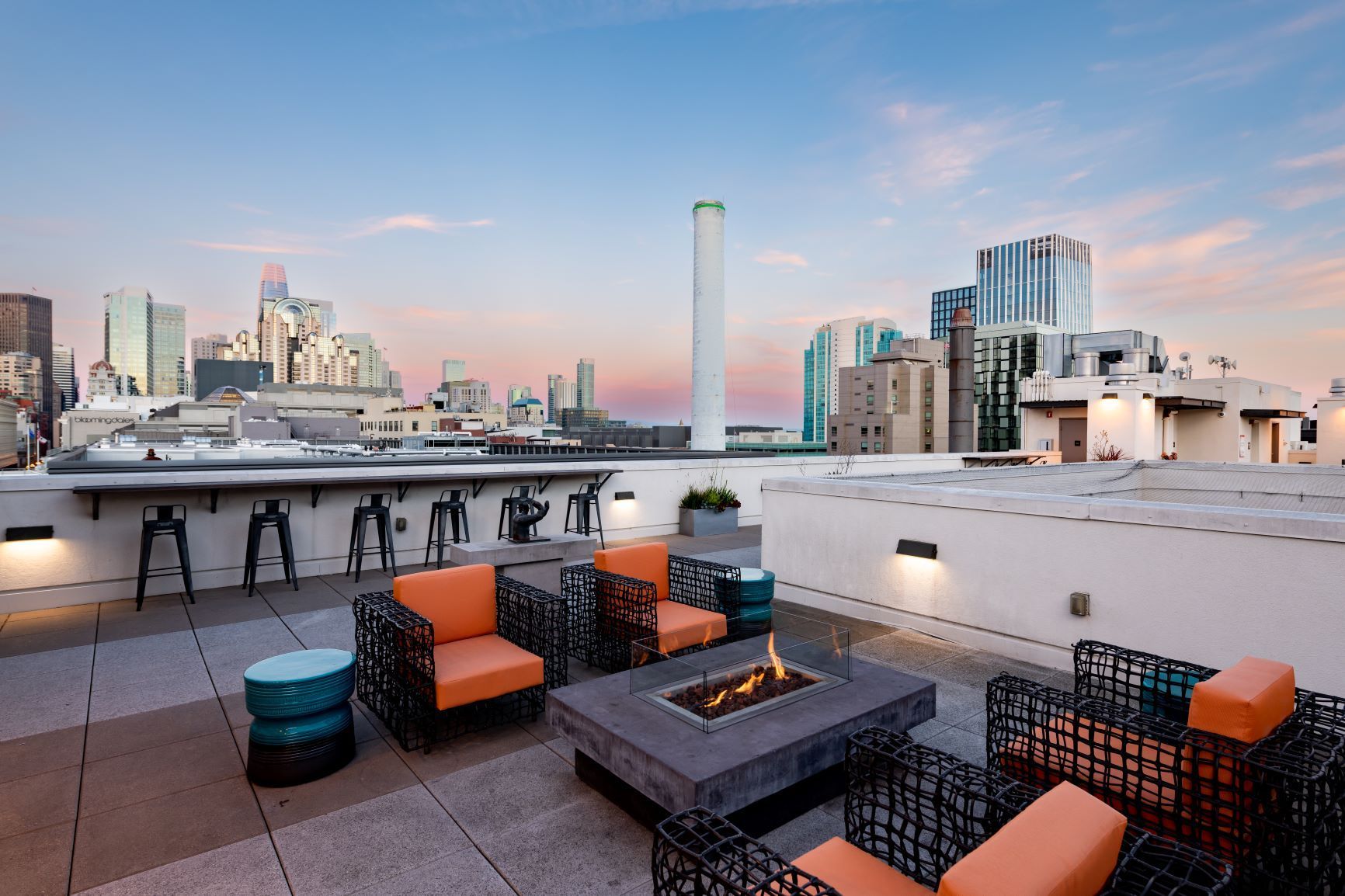Rooftop terrace with orange seating and fire pit overlooking a city skyline at dusk
