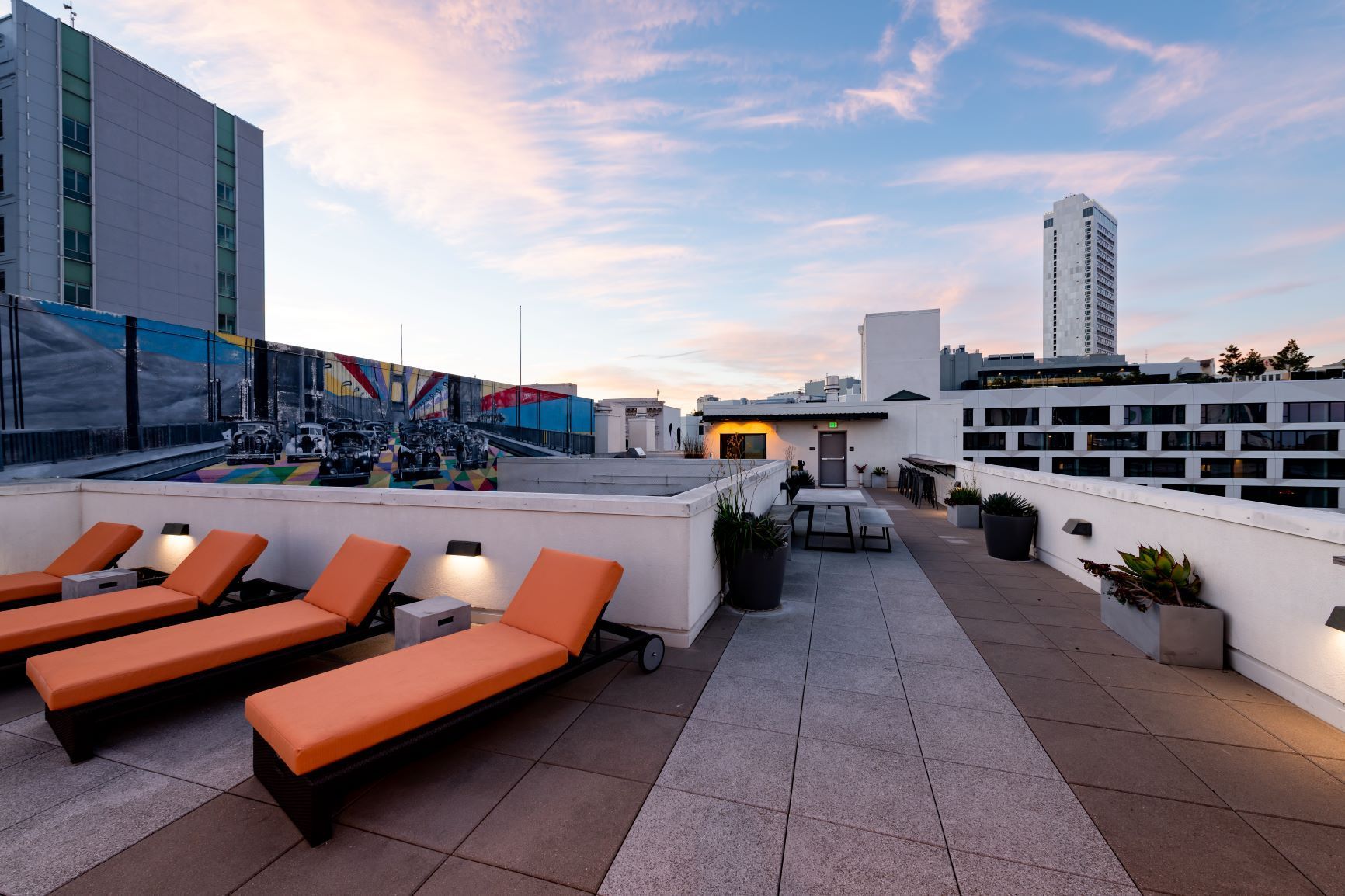 Rooftop terrace with orange loungers, city skyline, and pastel sunset sky