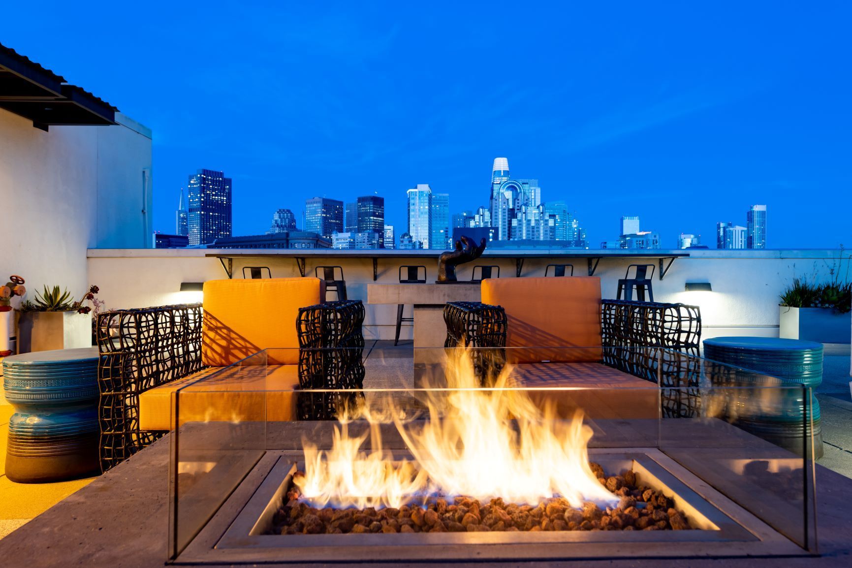 Rooftop lounge with fire pit and city skyline at dusk