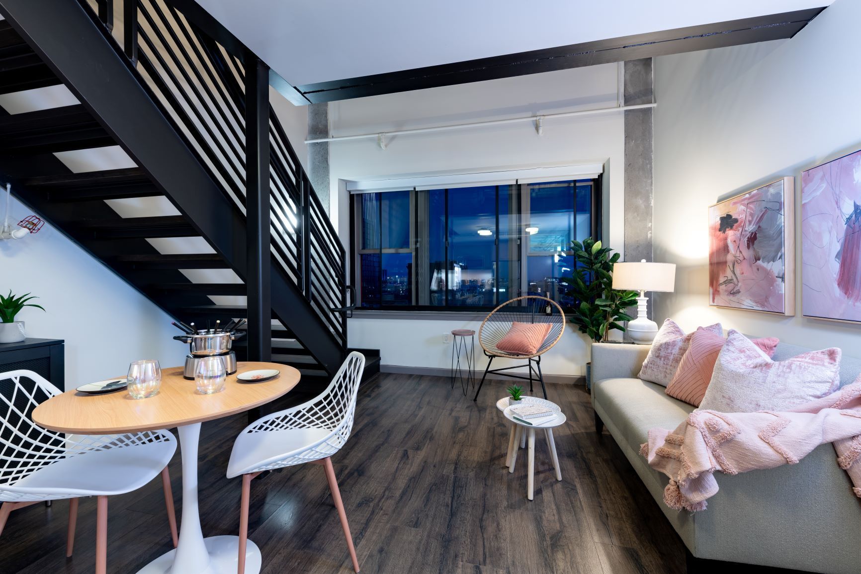 Modern loft living room with sofa, staircase, dining table, and city view through large window