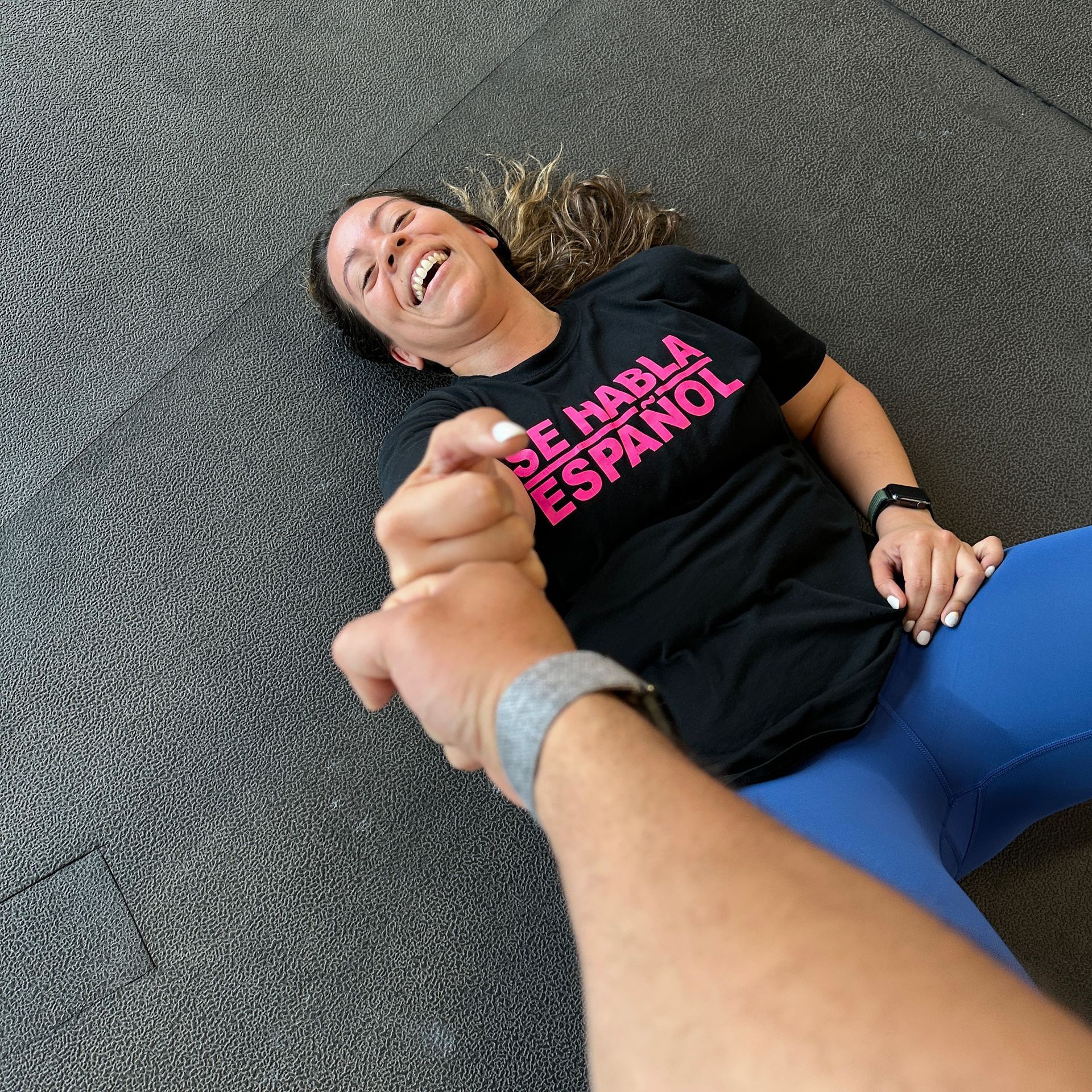 Woman in black shirt and blue leggings laughing while holding hand, on gray floor.