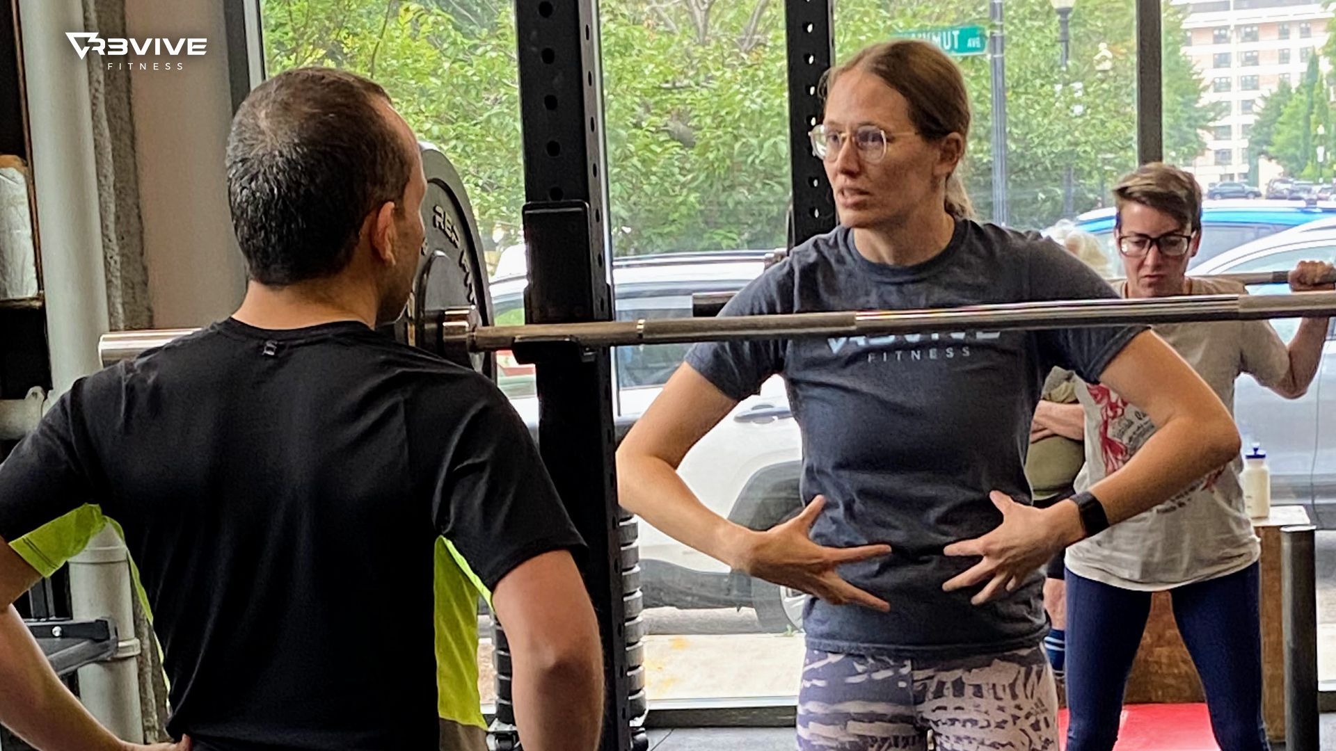 Woman coaching man and another on squats at gym.