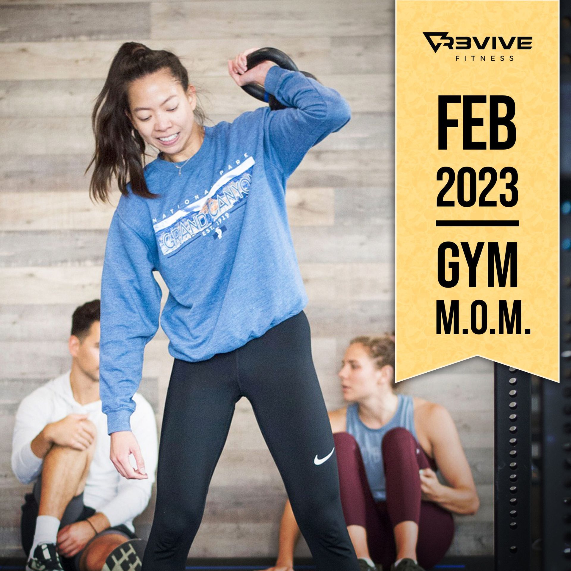Woman in blue sweatshirt swings kettlebell, smiling, at gym; others in background. 