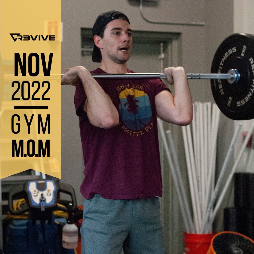 Man front squats at a gym; wearing cap, t-shirt, shorts. 