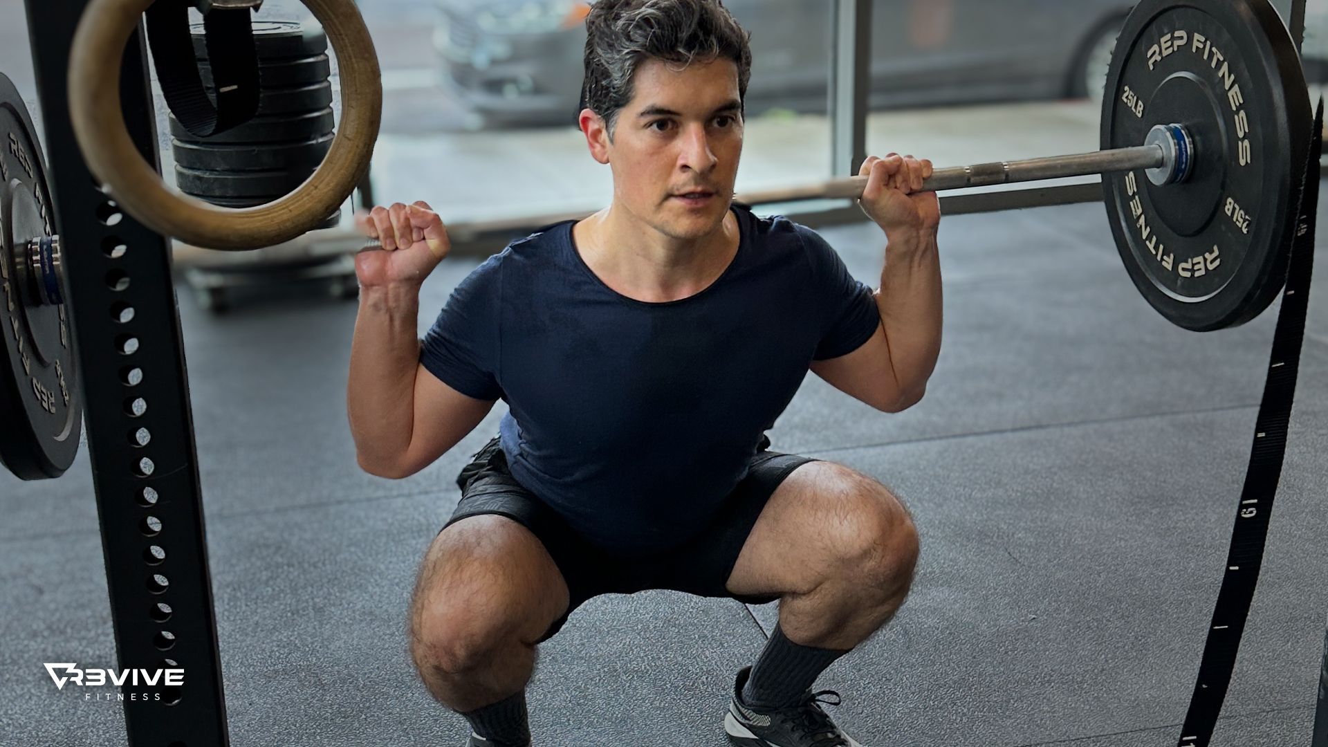 Man in a gym performing a squat with a barbell, focused expression.