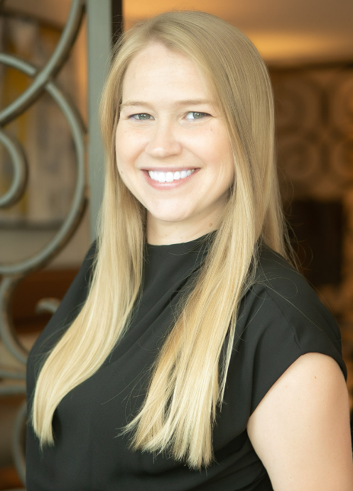 Smiling person with long blonde hair wearing a black top, standing indoors