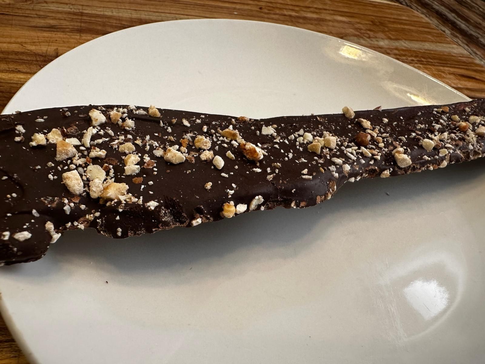 Chocolate-covered toffee bar with chopped nuts on a white plate.