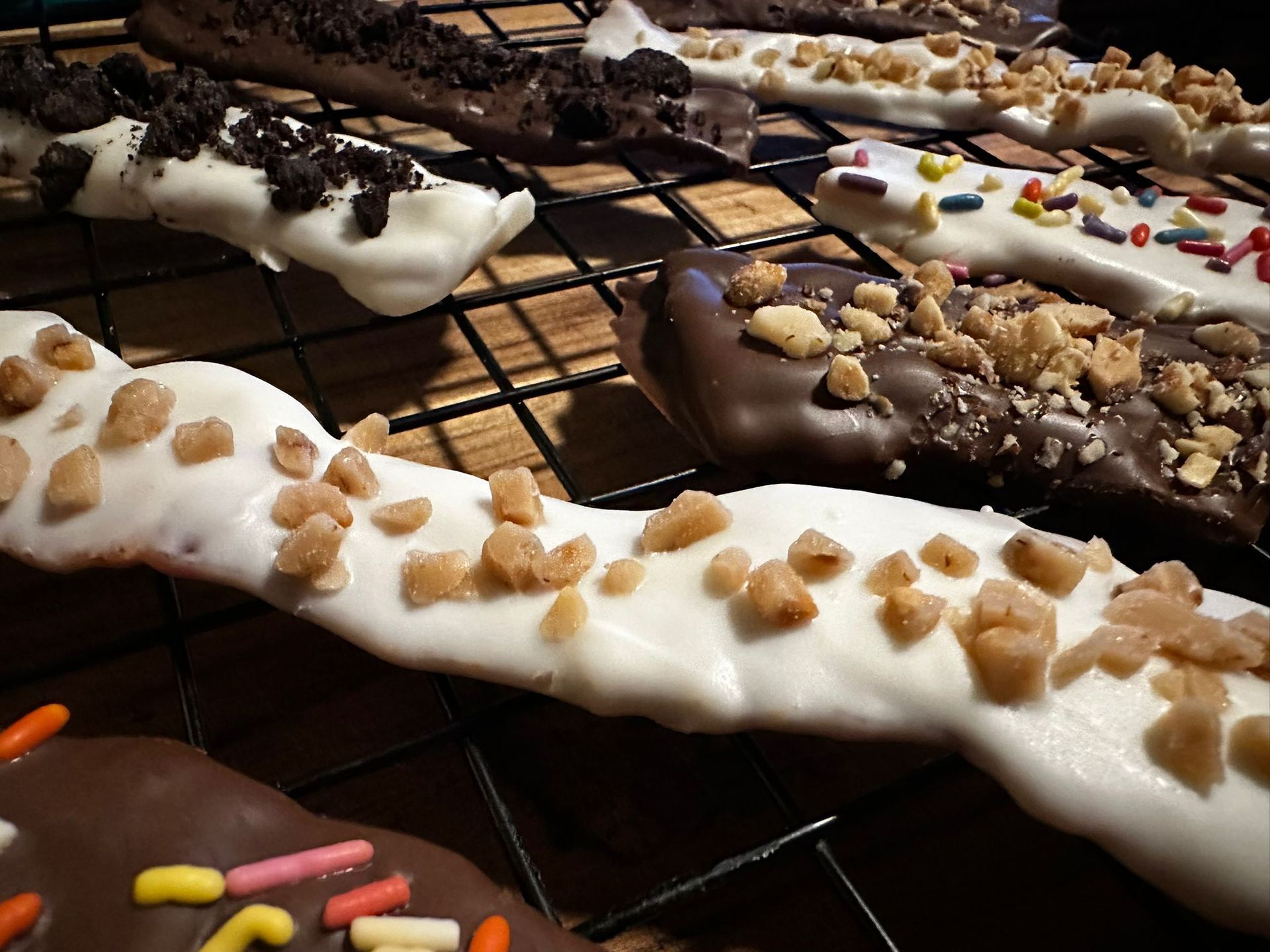 Chocolate-covered pretzel rods on a wire rack, with various toppings including cookies, nuts, and sprinkles.