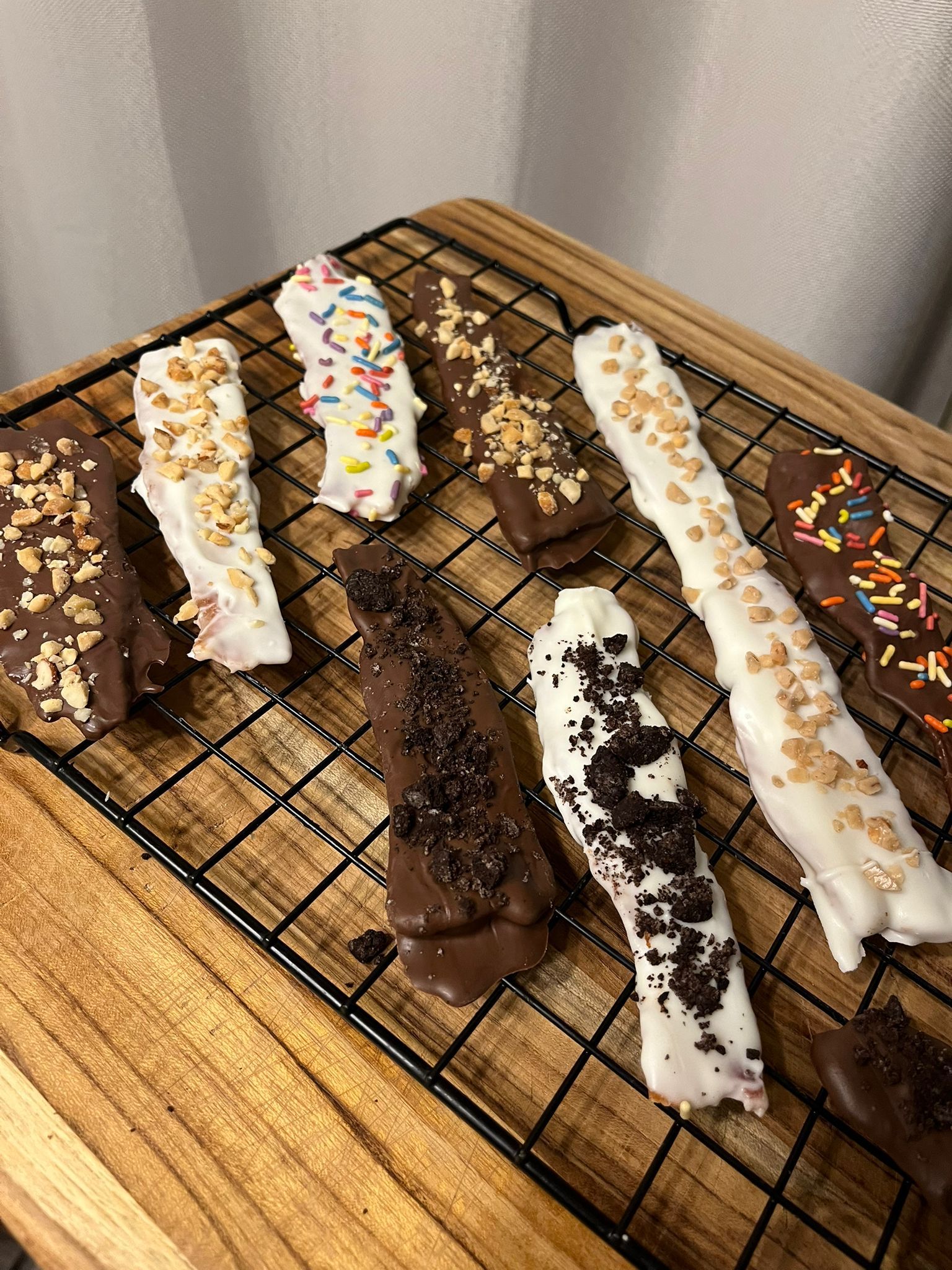 Chocolate-covered pretzel rods on a wire rack, drizzled with white and dark chocolate and various toppings.