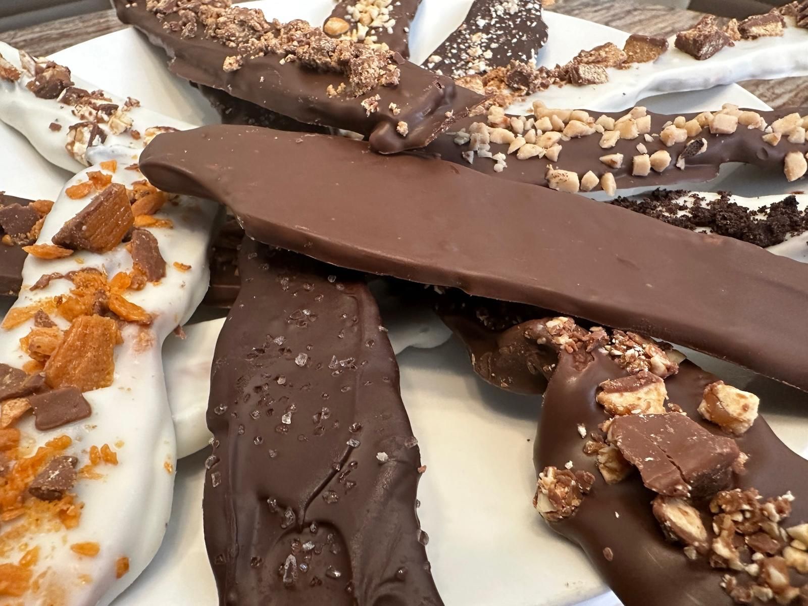 Close-up of assorted chocolate-covered toffee, some with nuts, on a white plate.