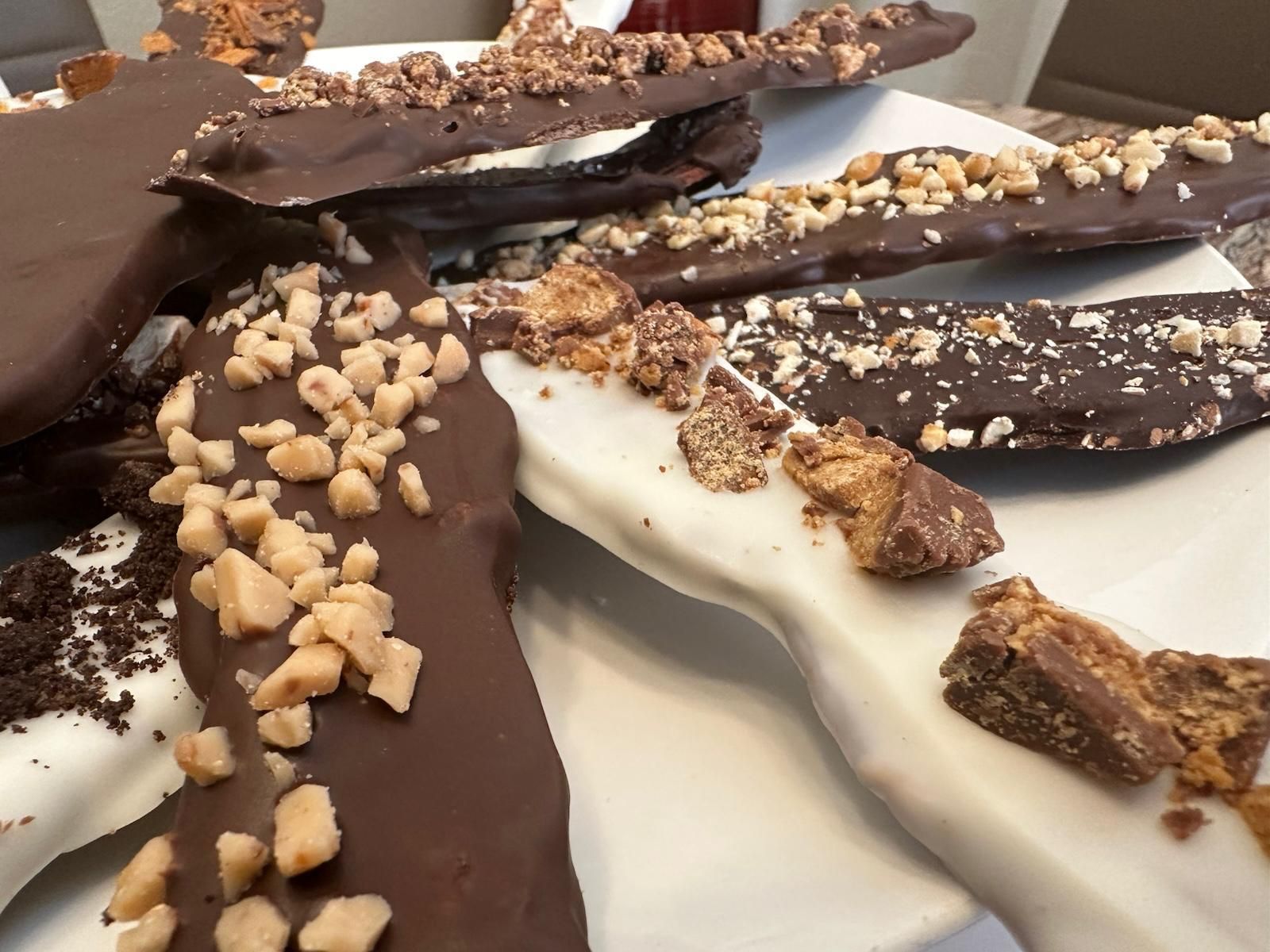 Chocolate-covered toffee bark pieces arranged on a plate; some are white chocolate, some dark, all with toppings.