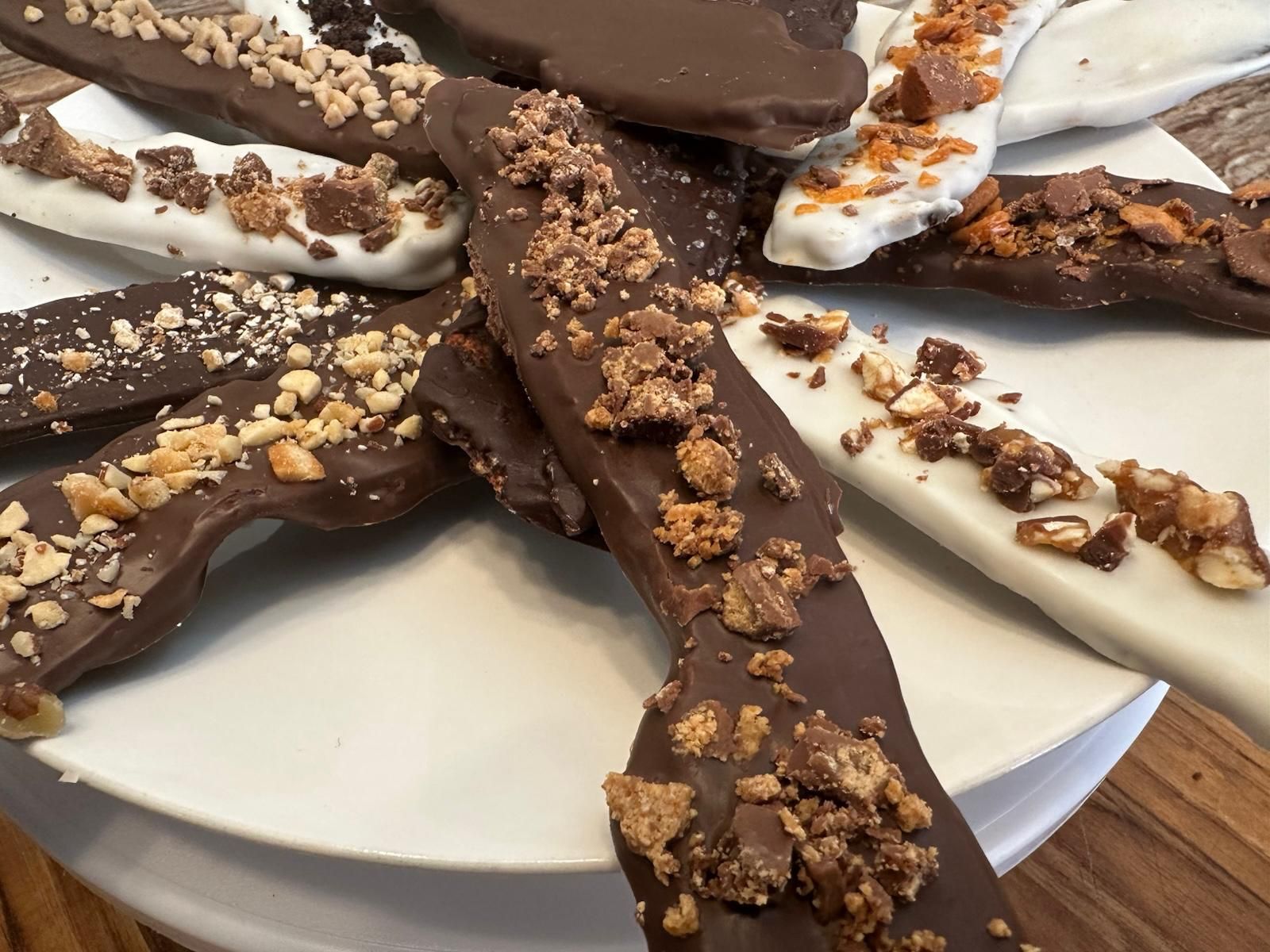 Chocolate-covered toffee pretzel crisps on a white plate, various toppings and dark and white chocolate.
