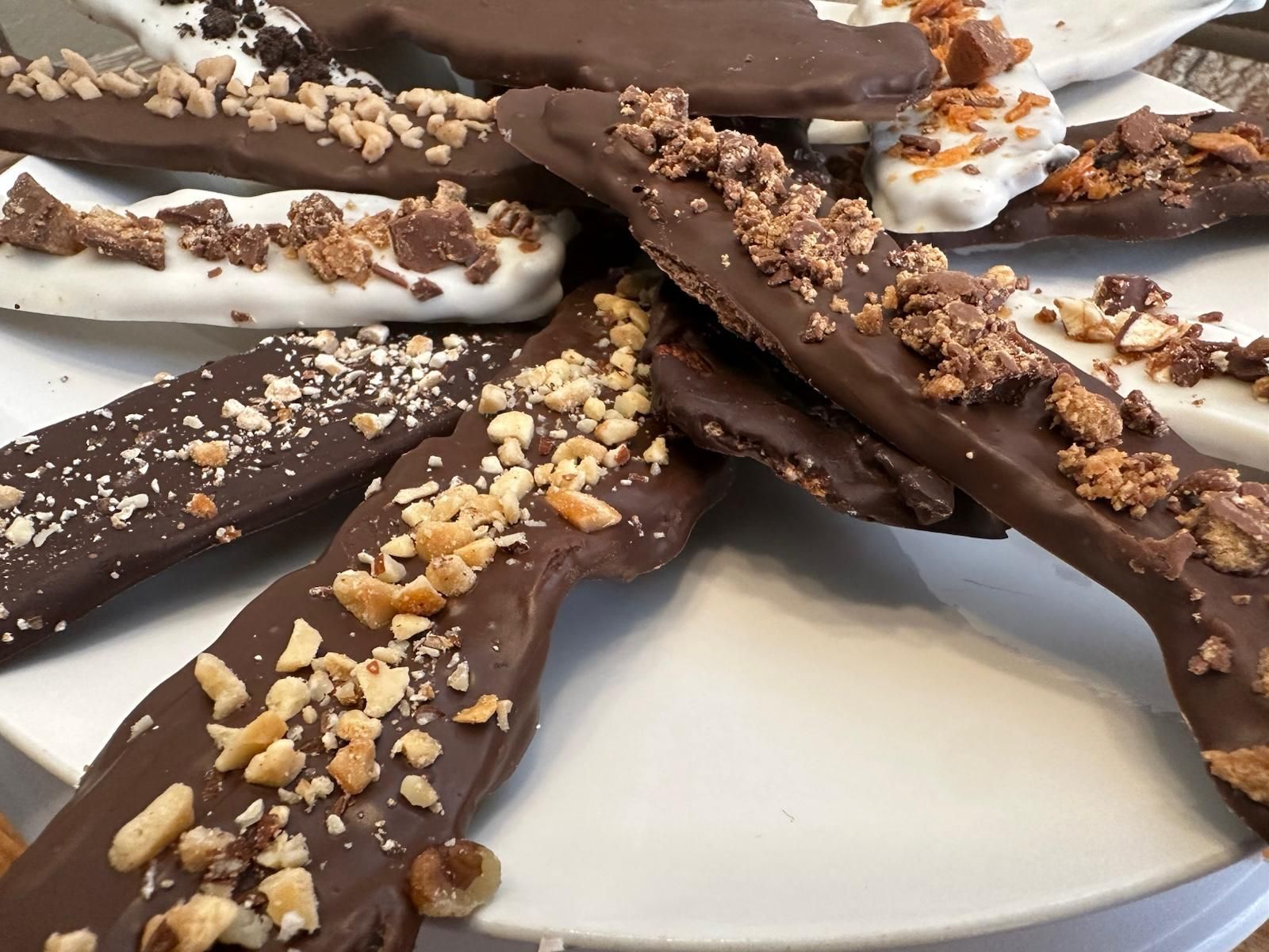 Chocolate-covered toffee, piled on a white plate, sprinkled with nuts and toffee bits.