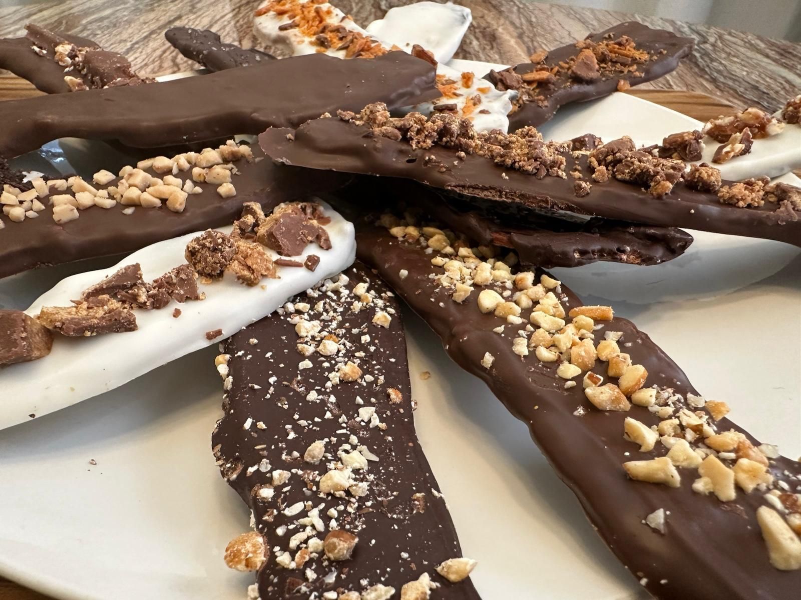 Chocolate-covered pretzel sticks, some white and dark chocolate with chopped nuts and toffee on a white plate.