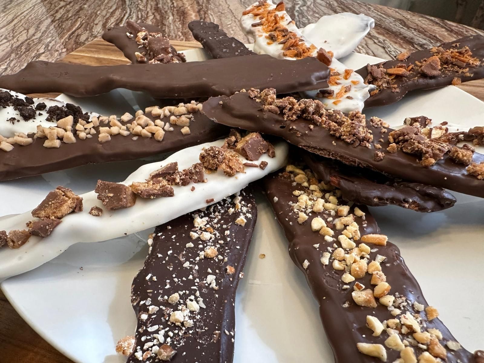 Chocolate-covered pretzel rods with various toppings, arranged on a white plate.