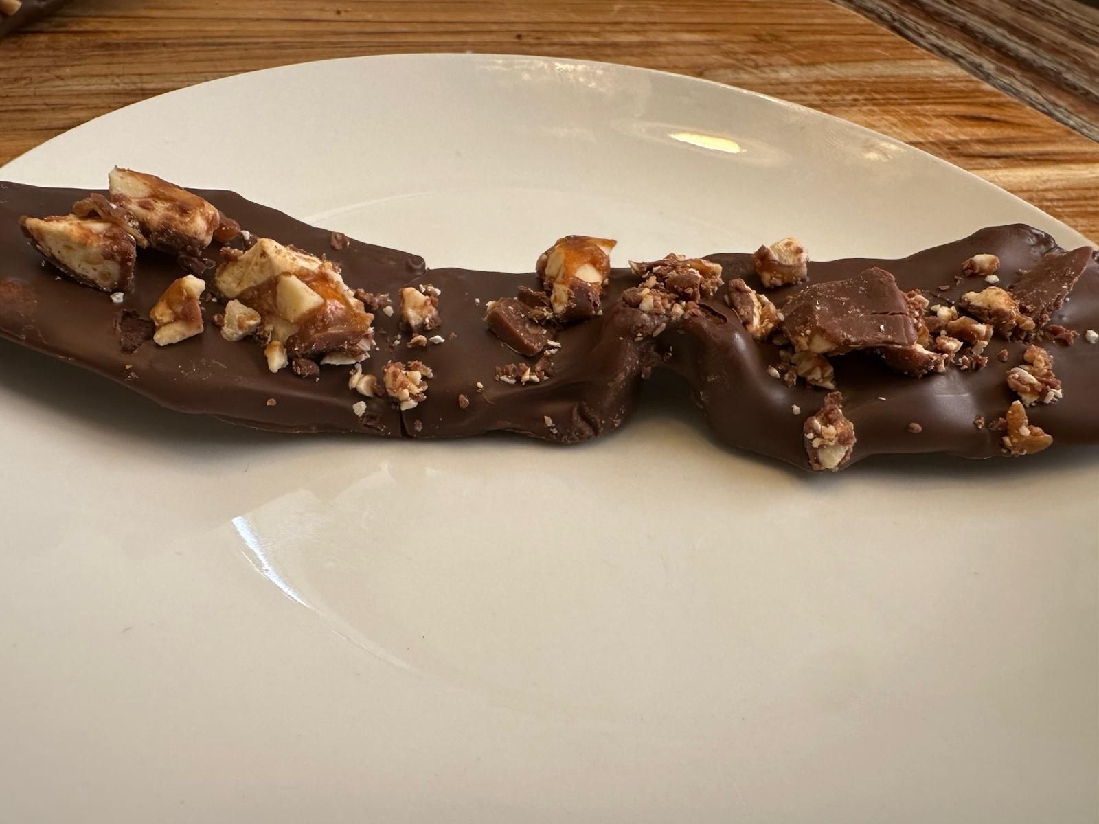 Chocolate-covered banana topped with chopped nuts on a white plate.