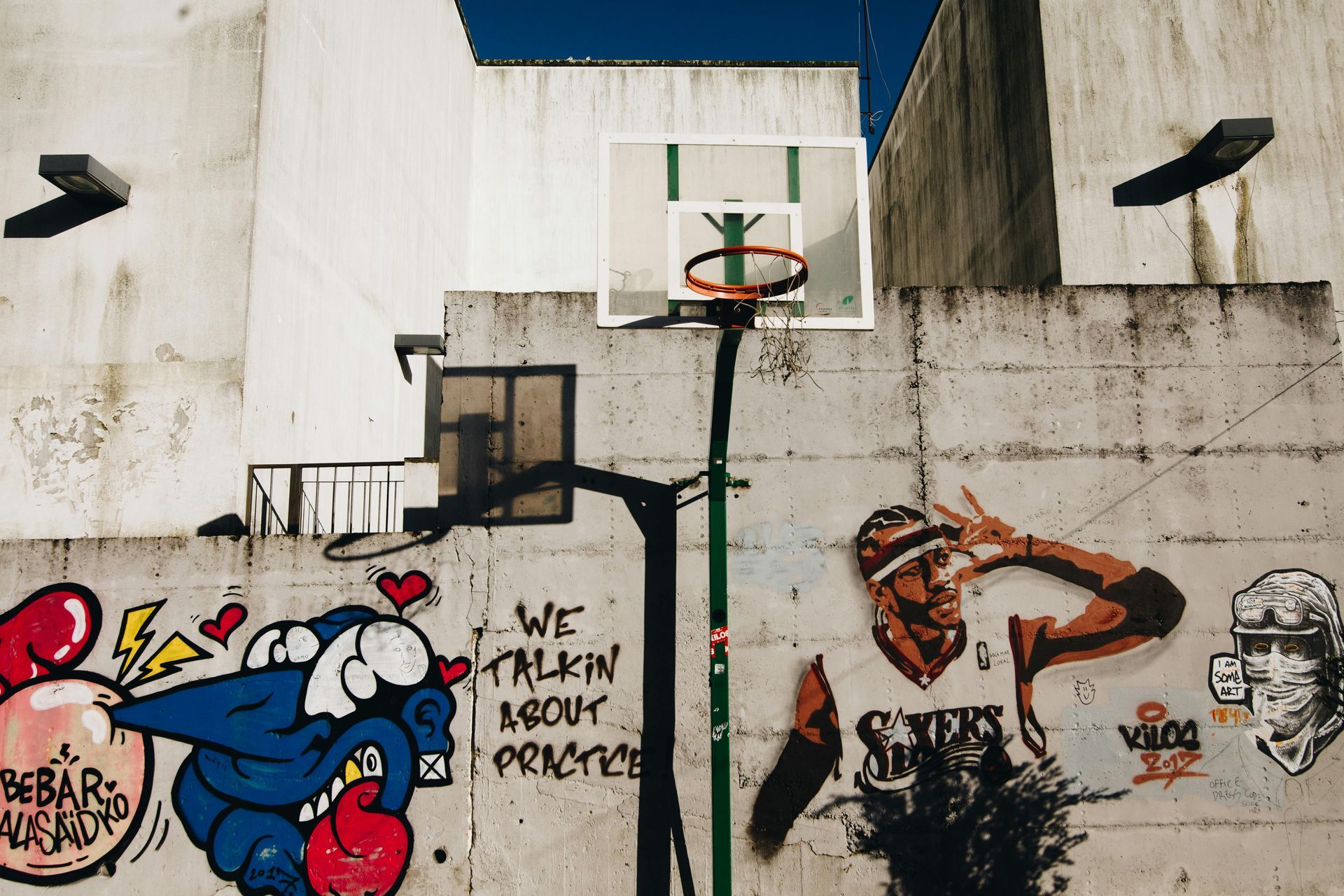 Basketball hoop on a graffiti-covered wall featuring a Kobe Bryant mural, in an urban setting.
