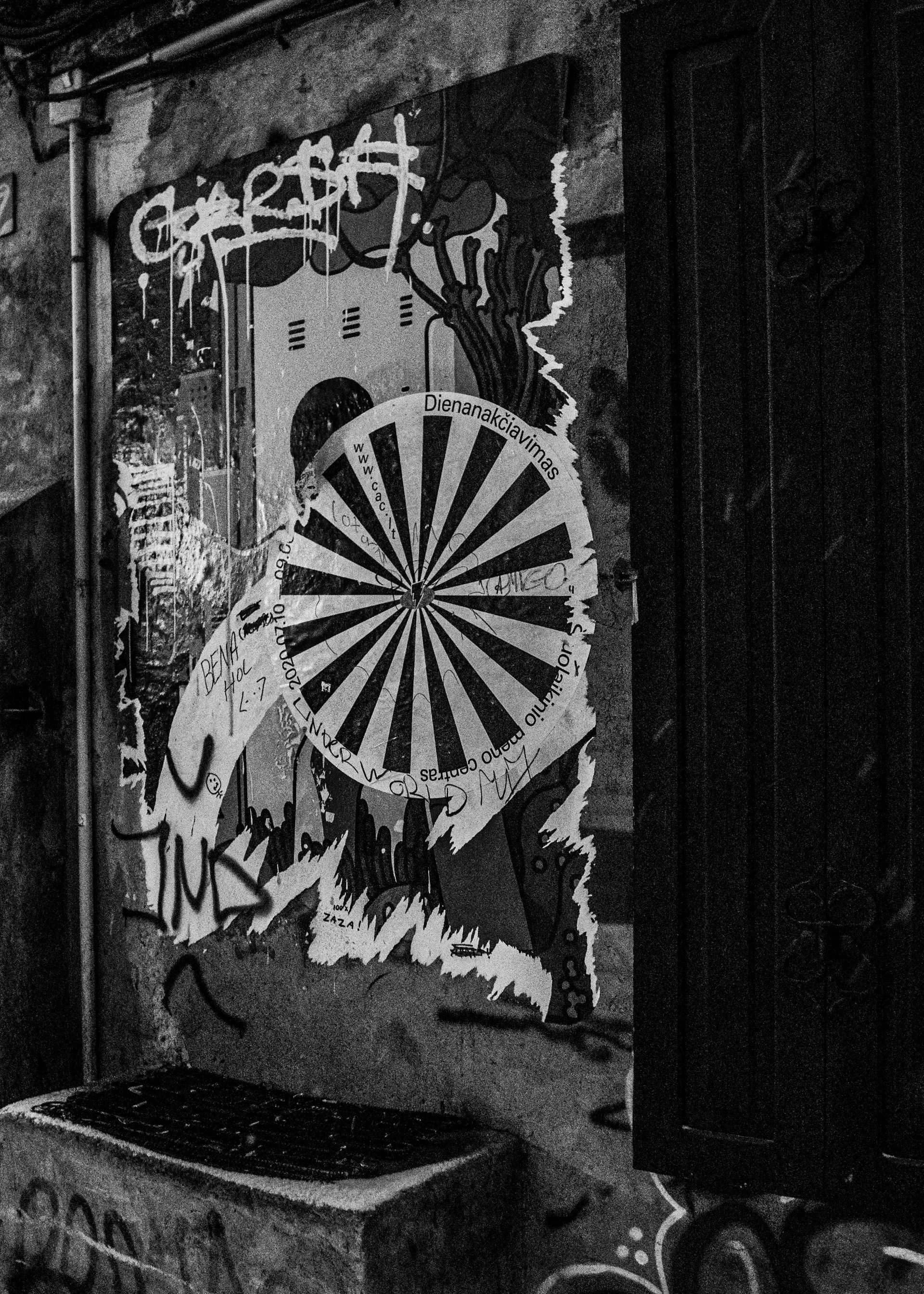 Black and white street art: a figure with a striped umbrella, graffiti on a brick wall next to a door.