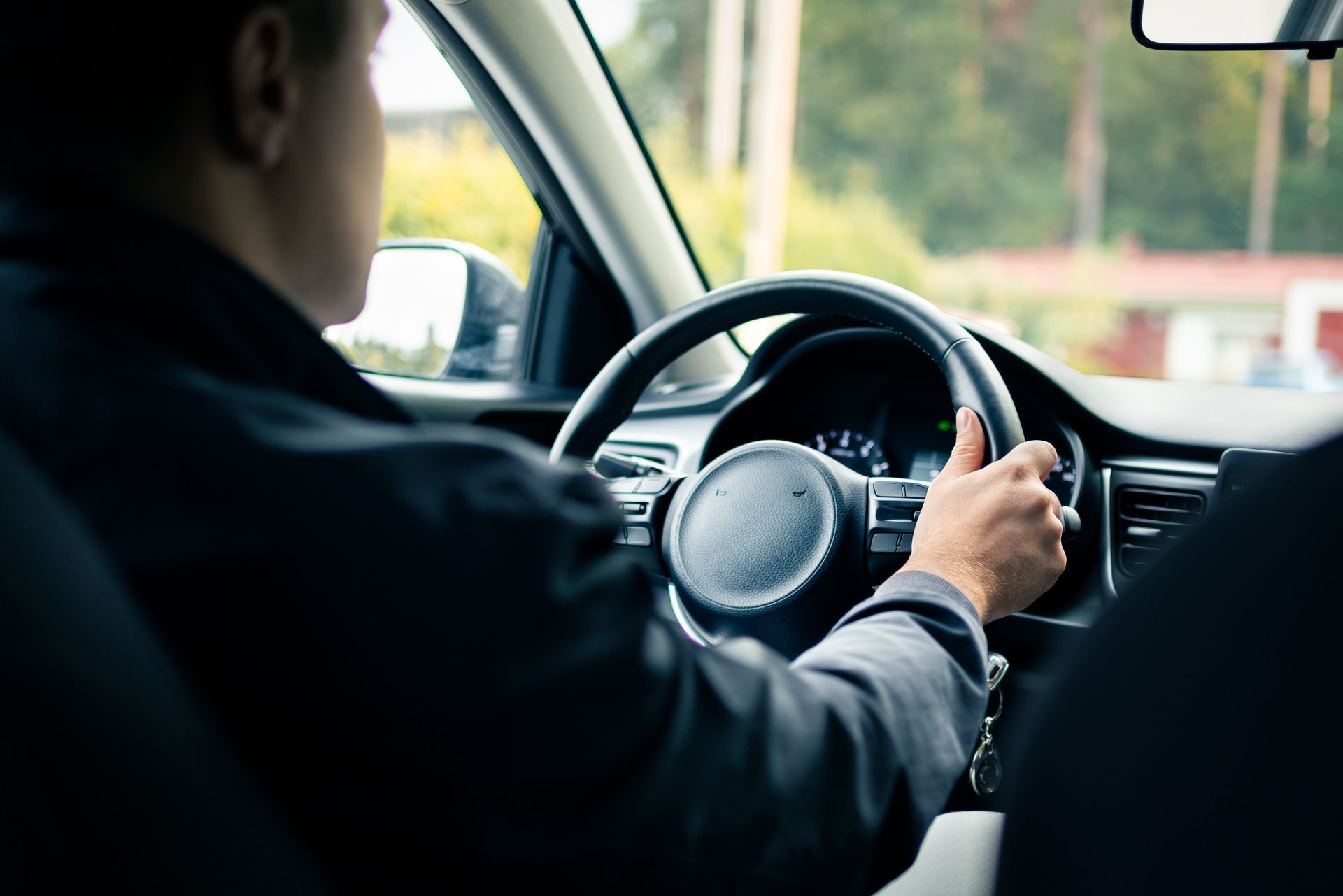 Man driving car holding steering wheel with hand, rear view from back seat perspective.