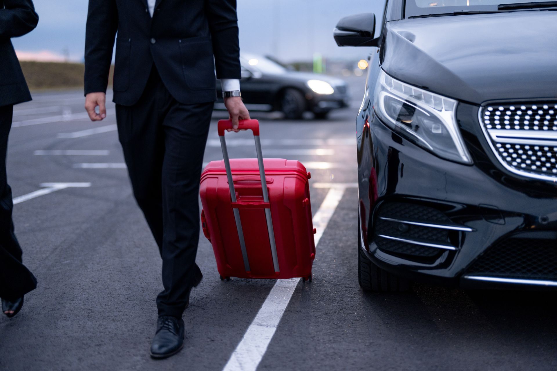 A man in a suit and tie walks confidently next to an SUV while pulling a suitcase behind him A man in a suit and tie walks confidently next to an SUV while pulling a suitcase behind him