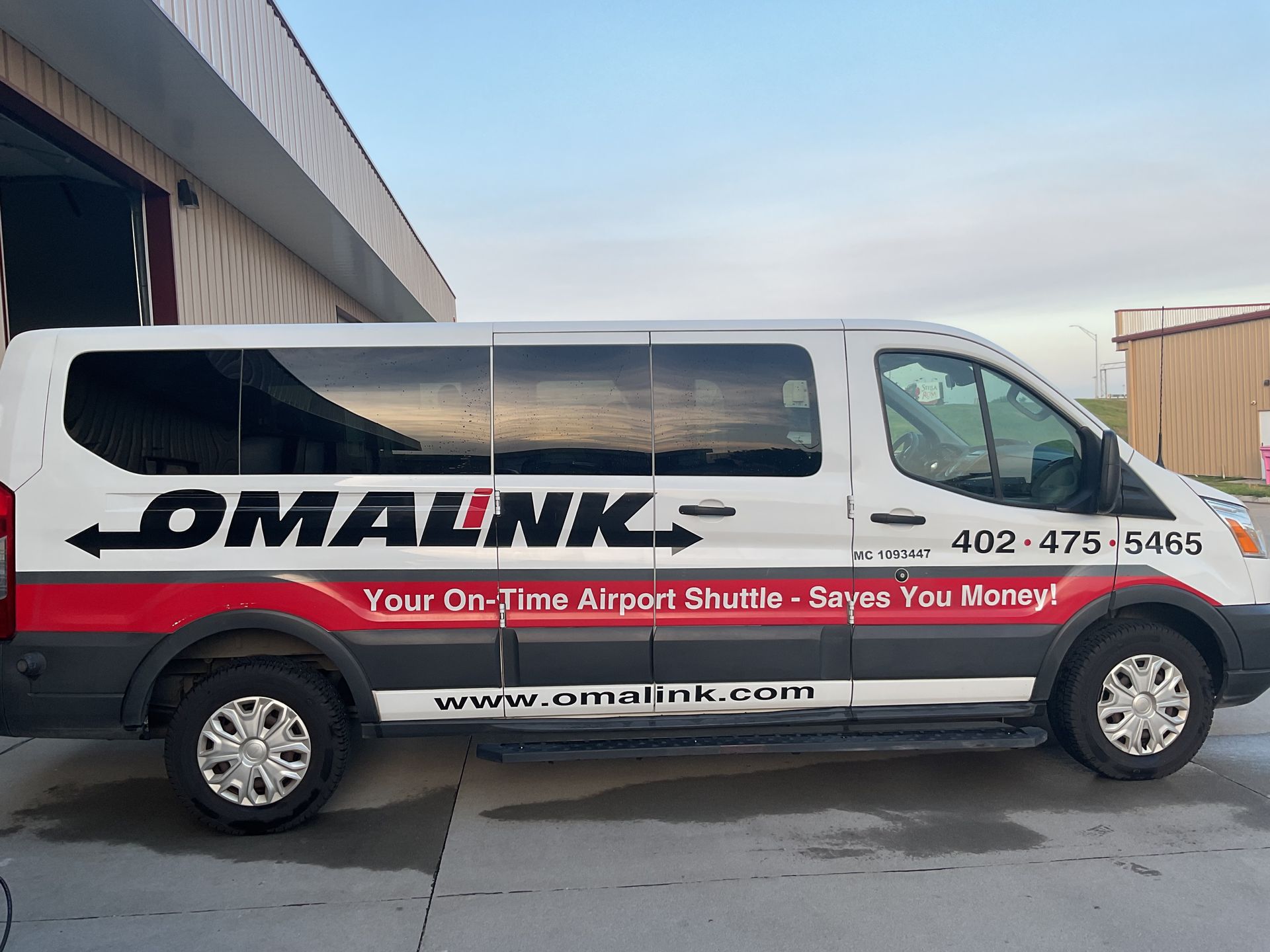 A side view of a white, black, and red Omalink passenger shuttle van parked on a concrete surface.