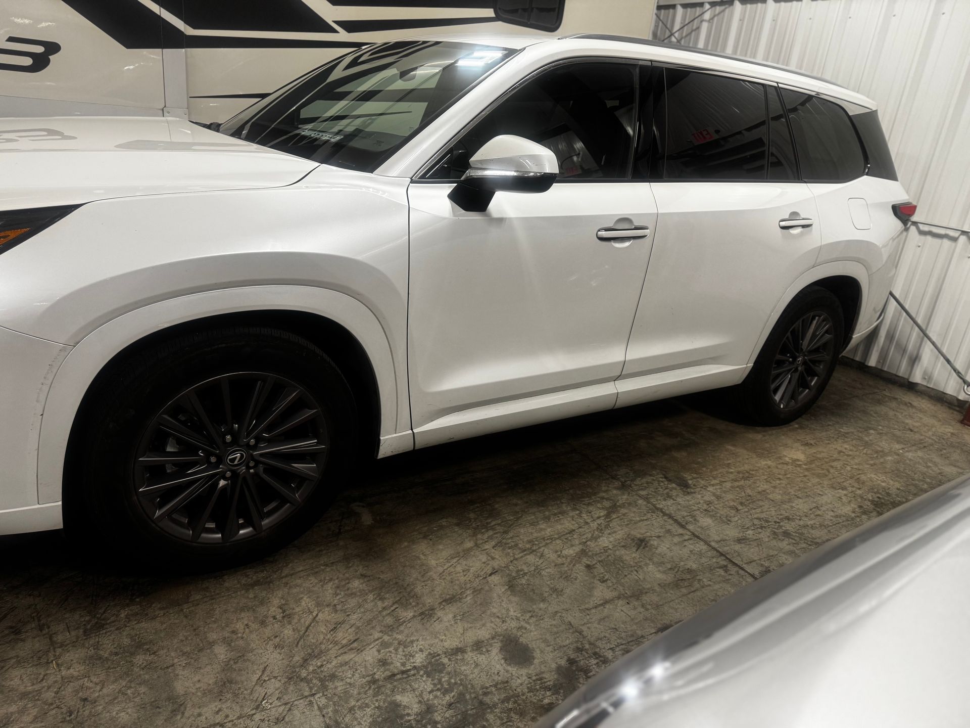 A white SUV with black alloy wheels parked indoors on a concrete floor.